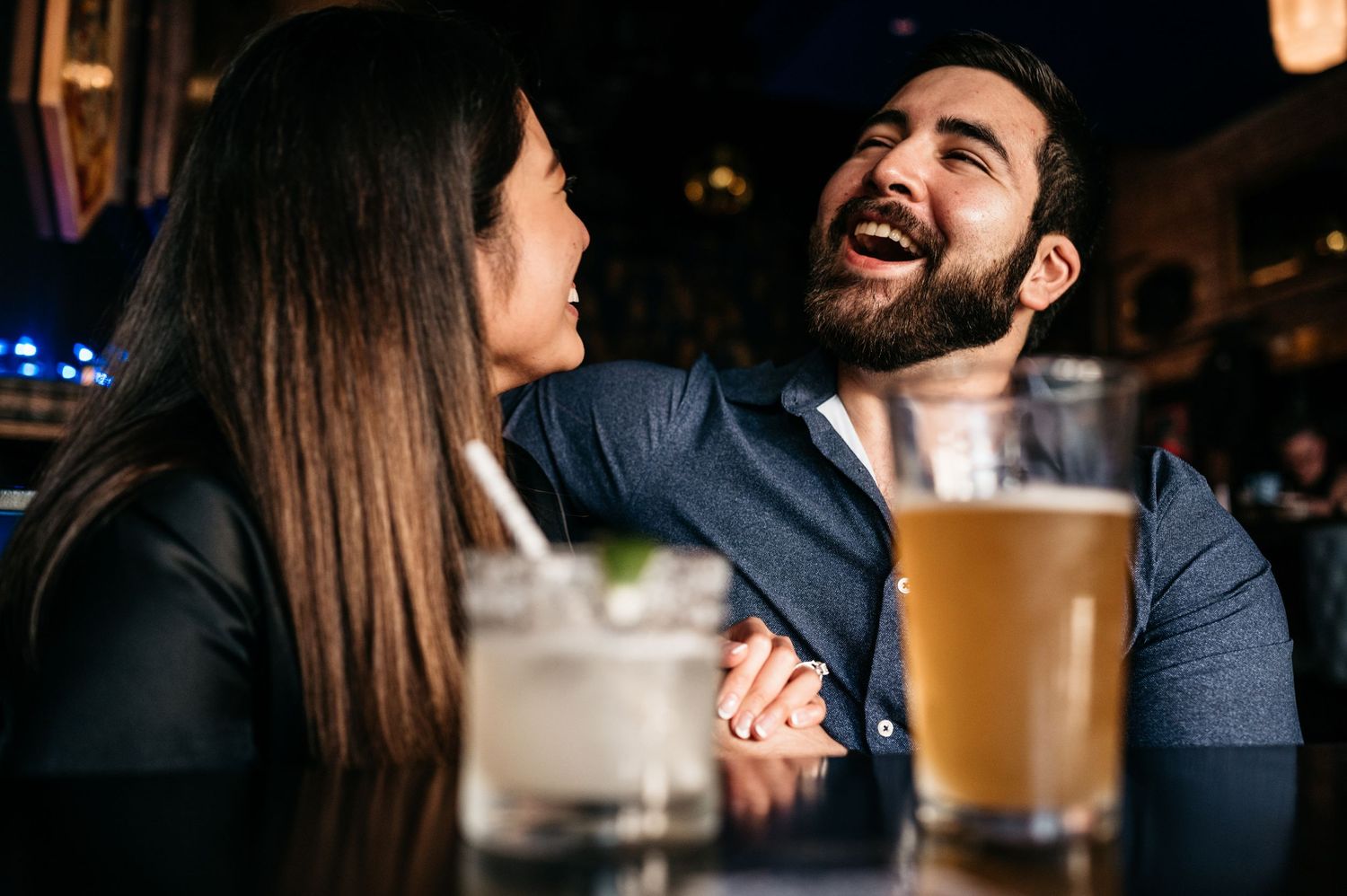 A couple shares a joyful moment while enjoying drinks at a bar.