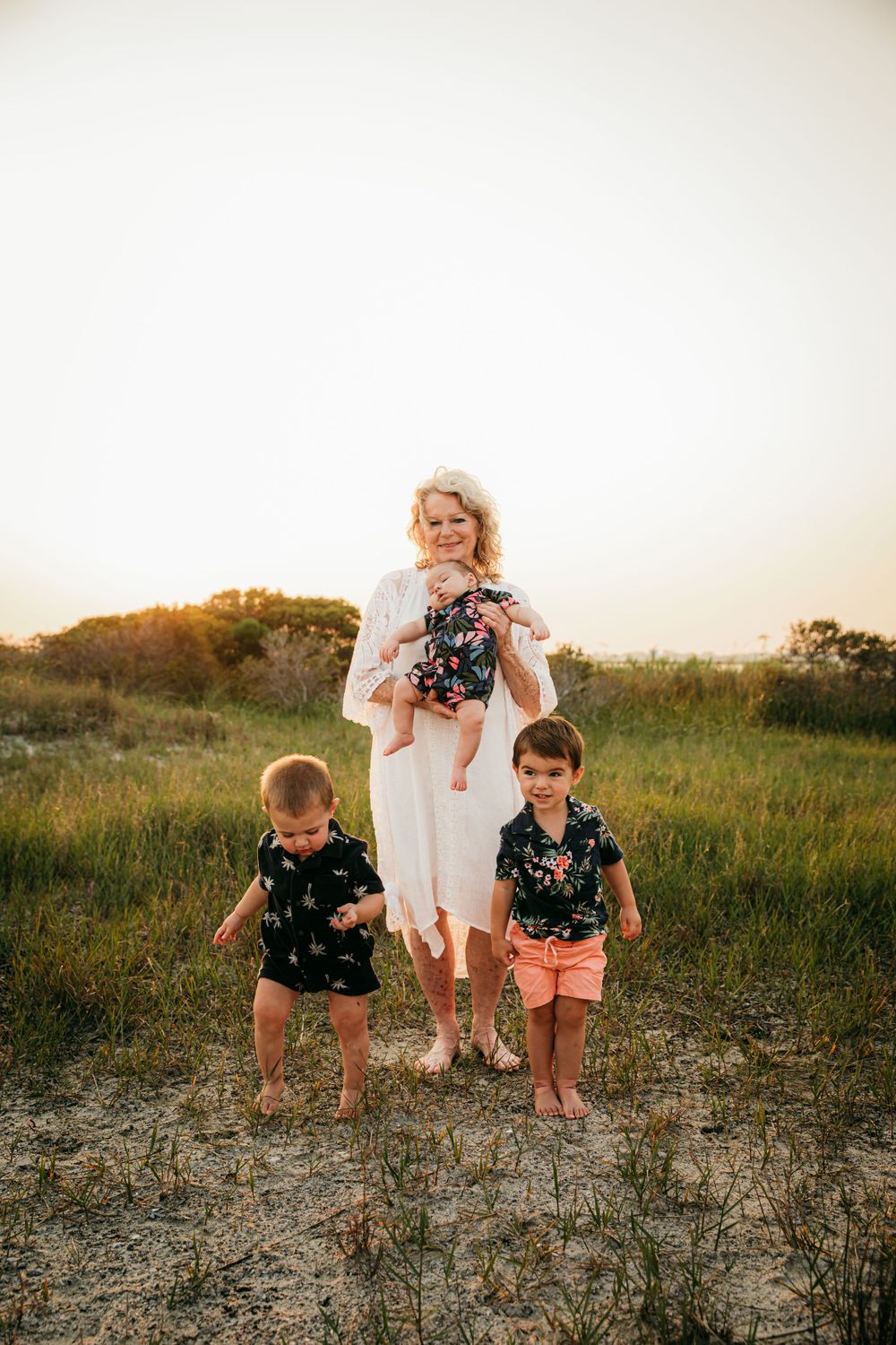 Family group poses in casual attire on grassy dunes during sunset golden hour.