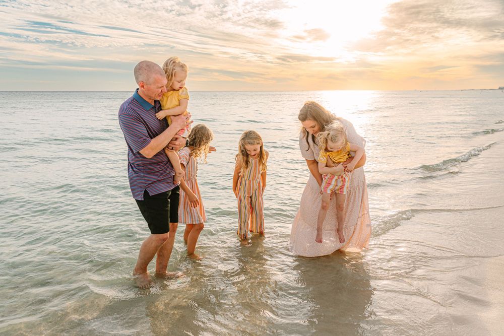 Family playing together in shallow ocean waves during golden hour sunset.