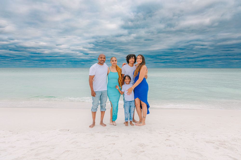 Beachgoers enjoying a sunny day on white sand with turquoise waters and cloudy sky.