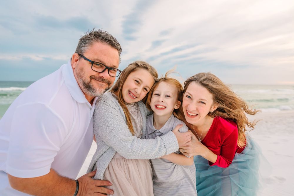 Family enjoying a playful moment together on a white sandy beach with ocean waves in background.