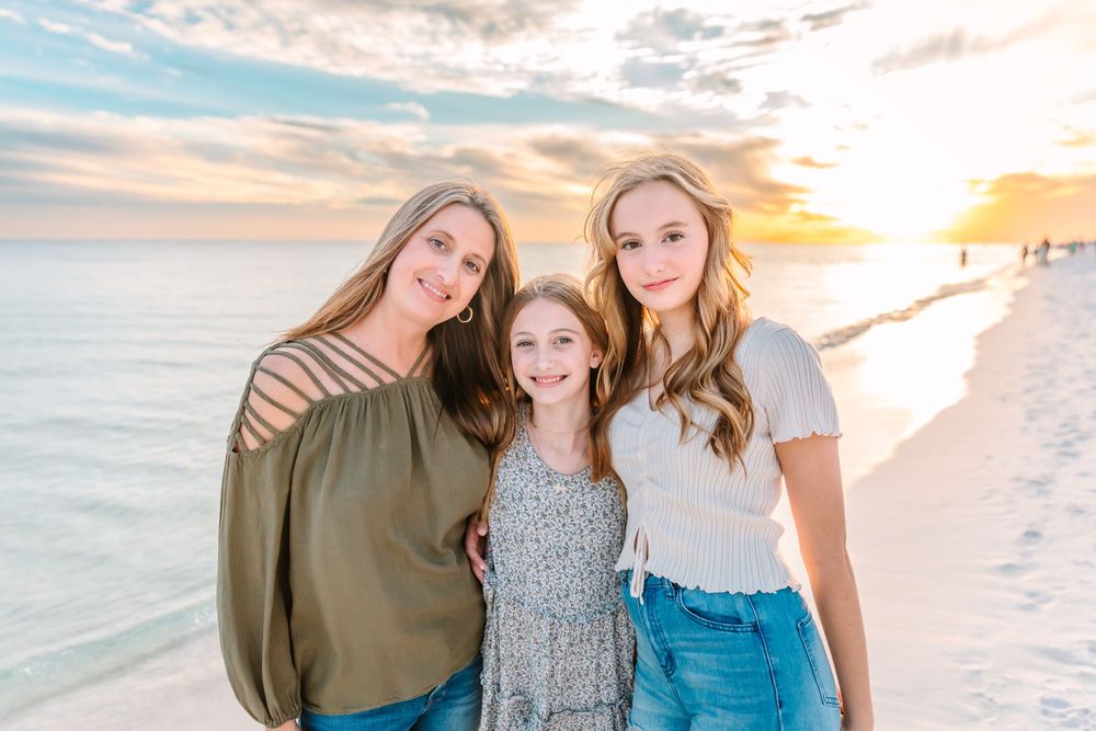 Family poses together on a beautiful beach at sunset with soft pastel sky in the background.