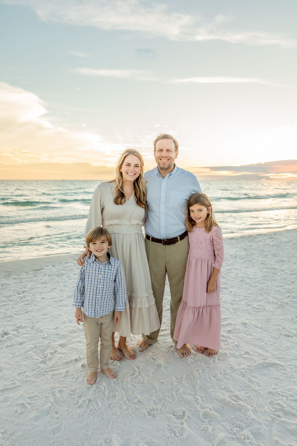 Family group photo on pristine white beach with ocean waves and sunset in background.
