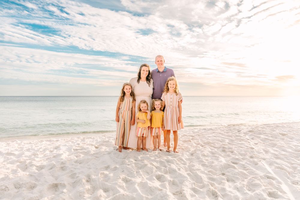 Family portrait series on beach with soft sunset lighting and ocean waves in background.