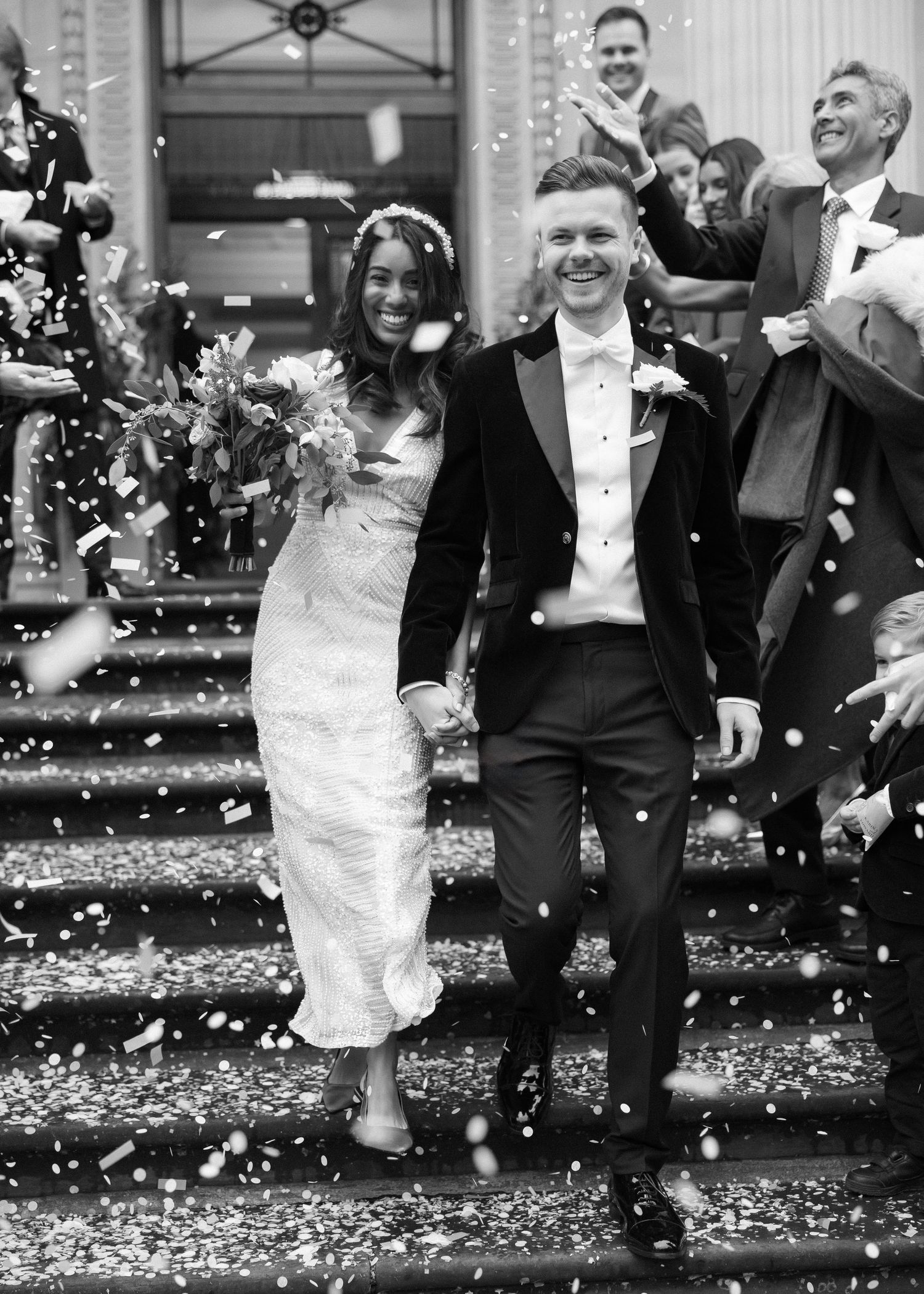 Black and white photo of newlyweds celebrating at a town hall wedding surrounded by falling confetti in London.