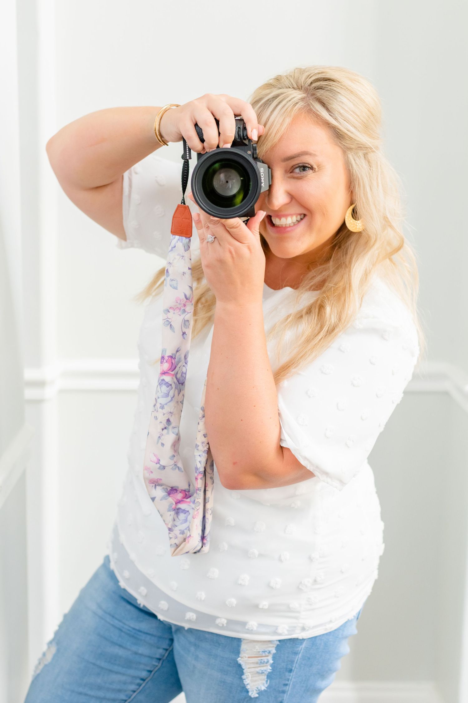 A smiling woman holding a camera and taking a photo. Katie Gibbons Photography