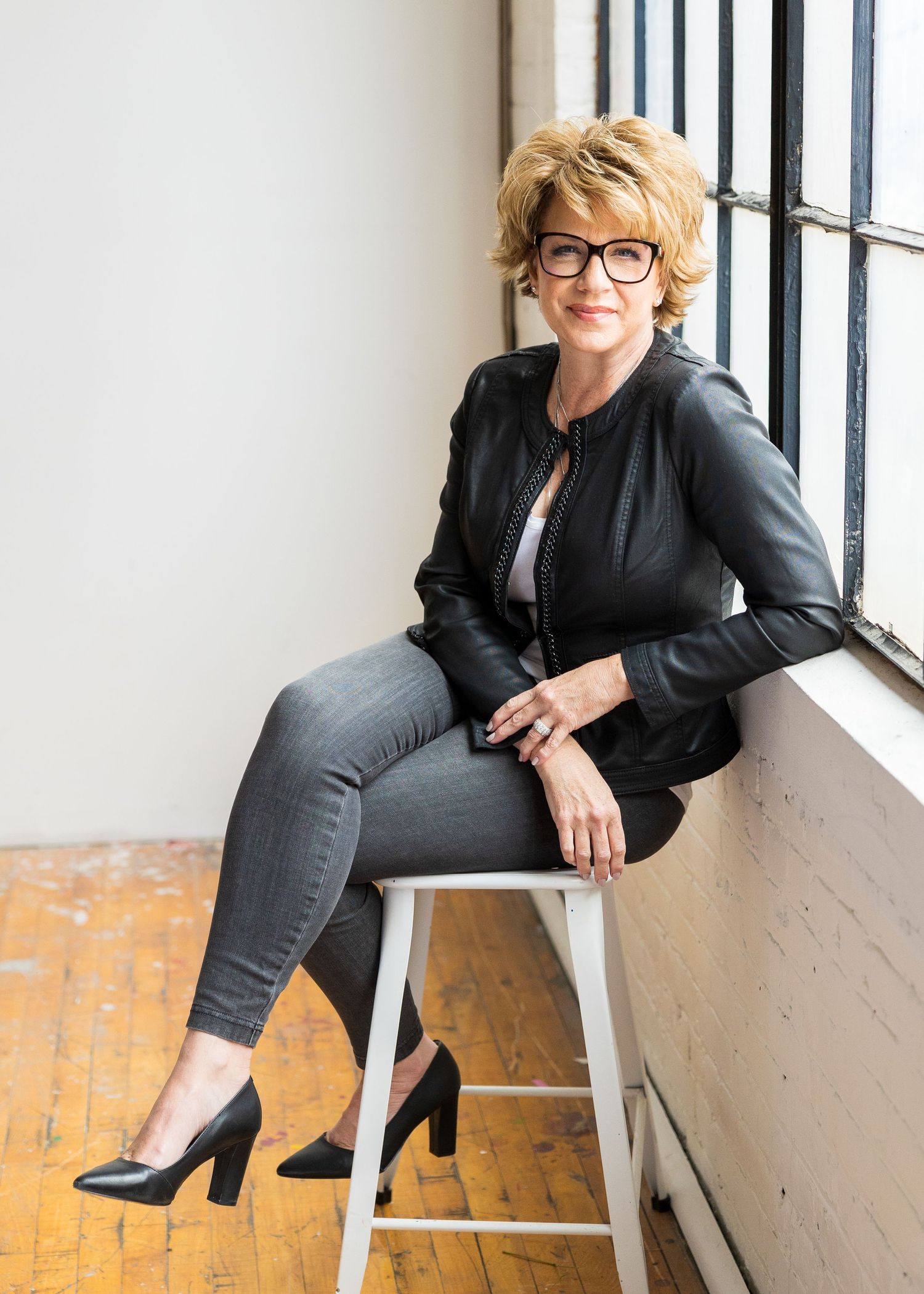 professional woman with glasses sitting on stool against window