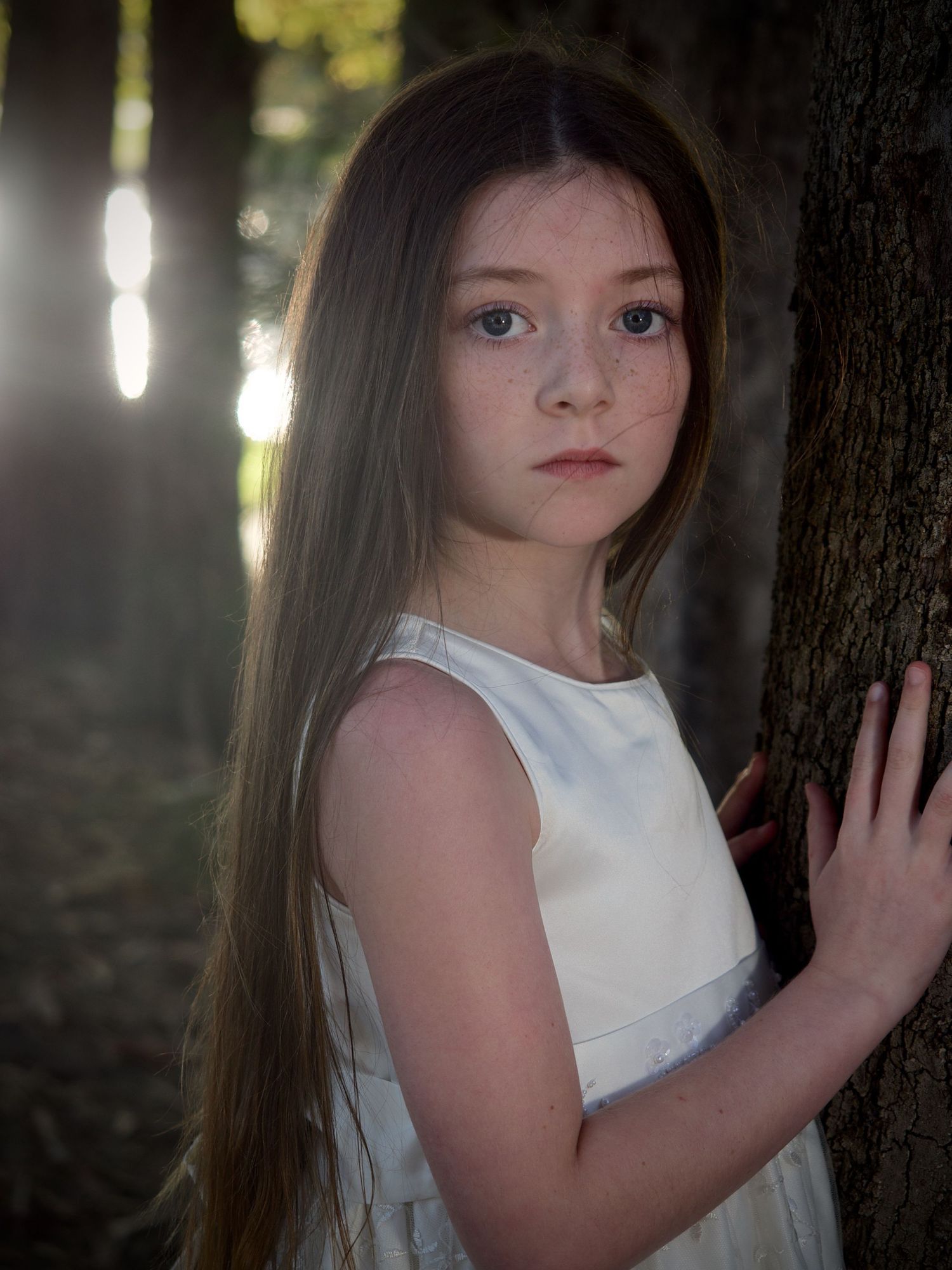 outdoor portrait of a young girl stand in the forest with sunlight coming through the trees