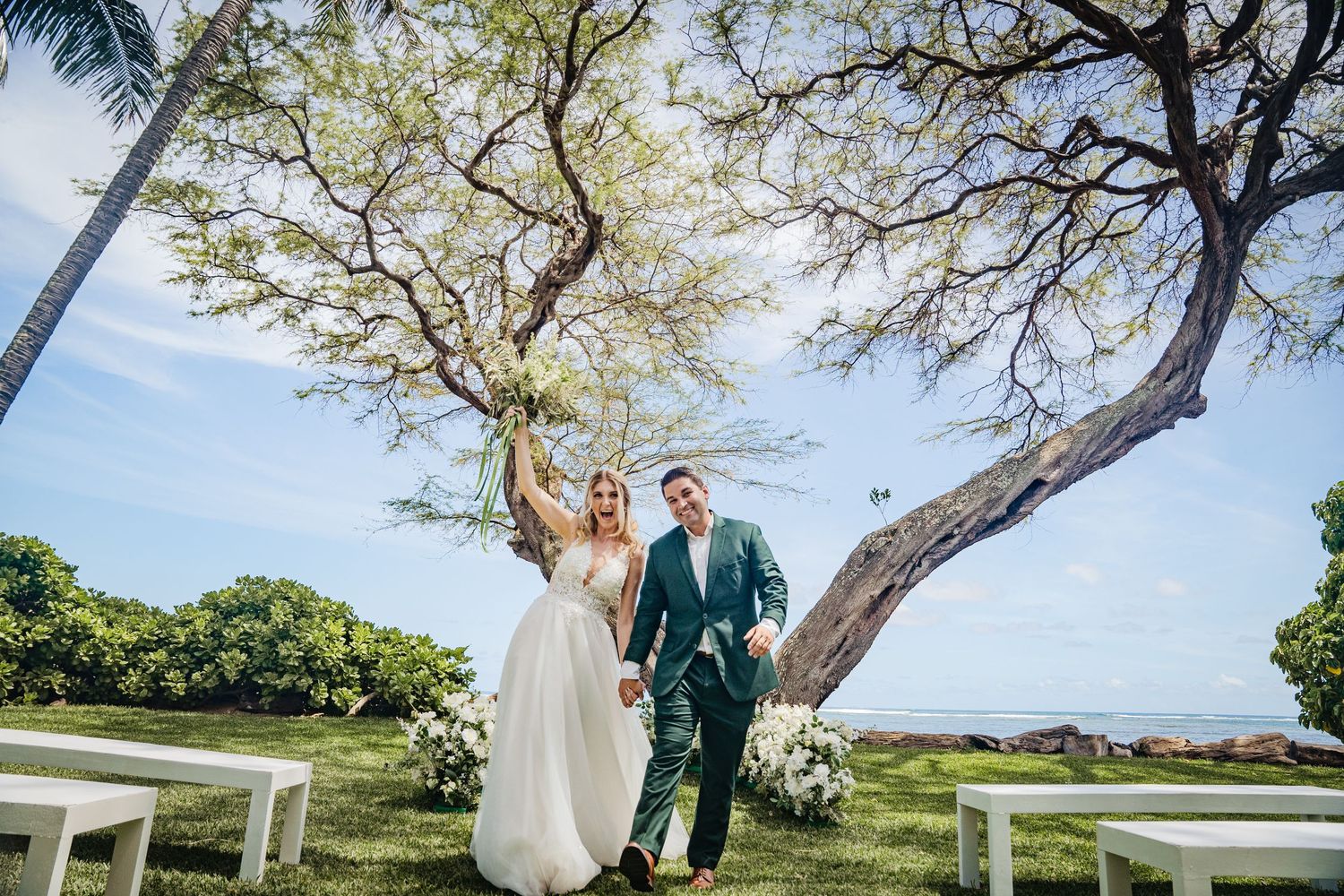 A romantic wedding portrait under a sprawling tree at a tropical beach venue.