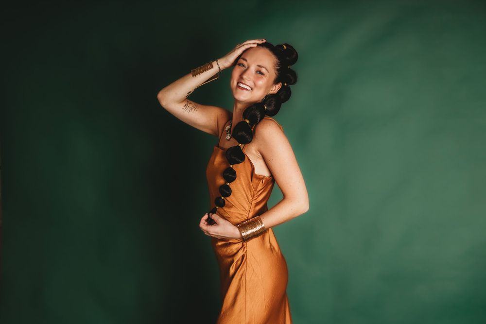 Dramatic fashion poses against dark green background in rust-colored outfit.