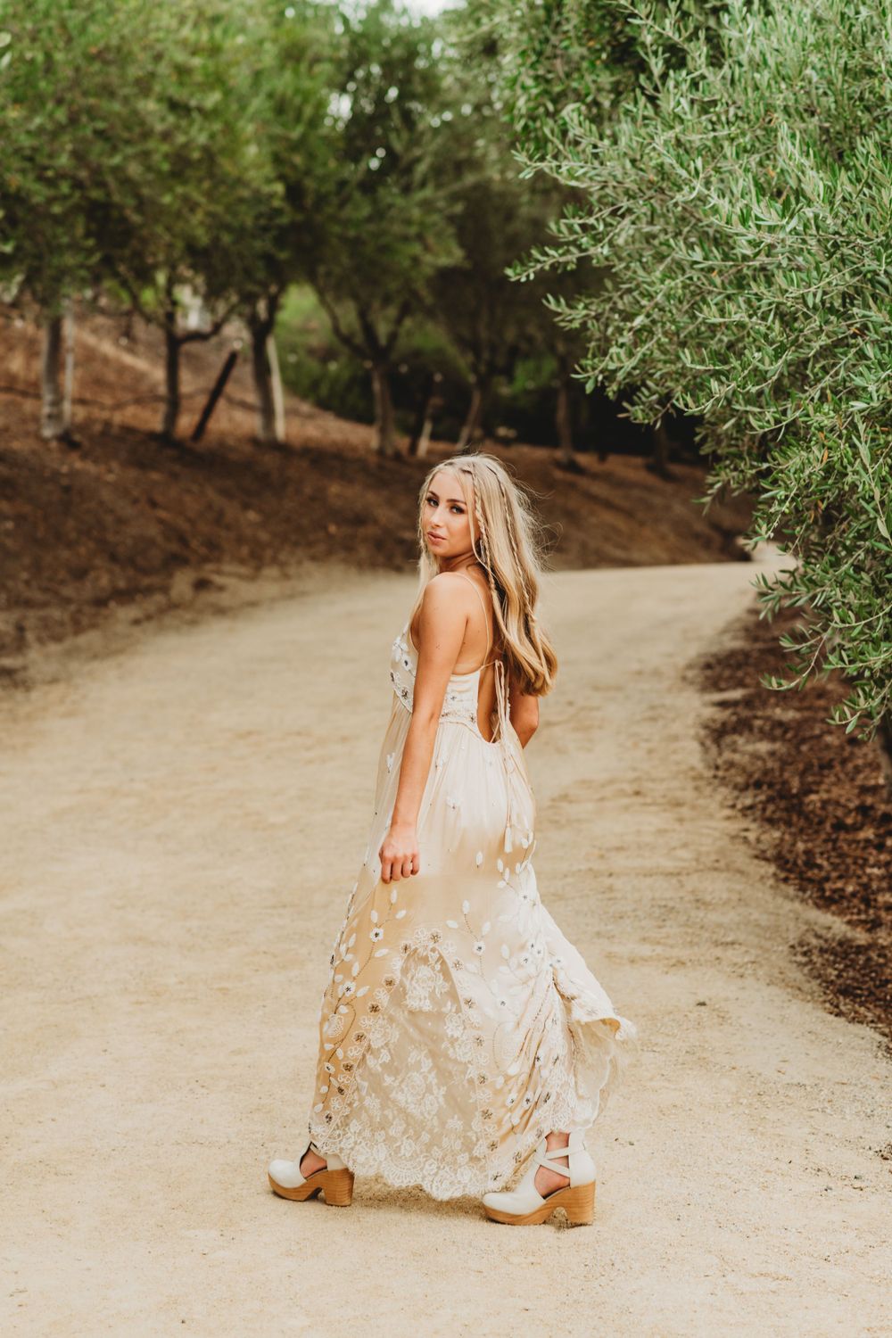 A romantic outdoor photoshoot on a dirt path surrounded by olive trees.