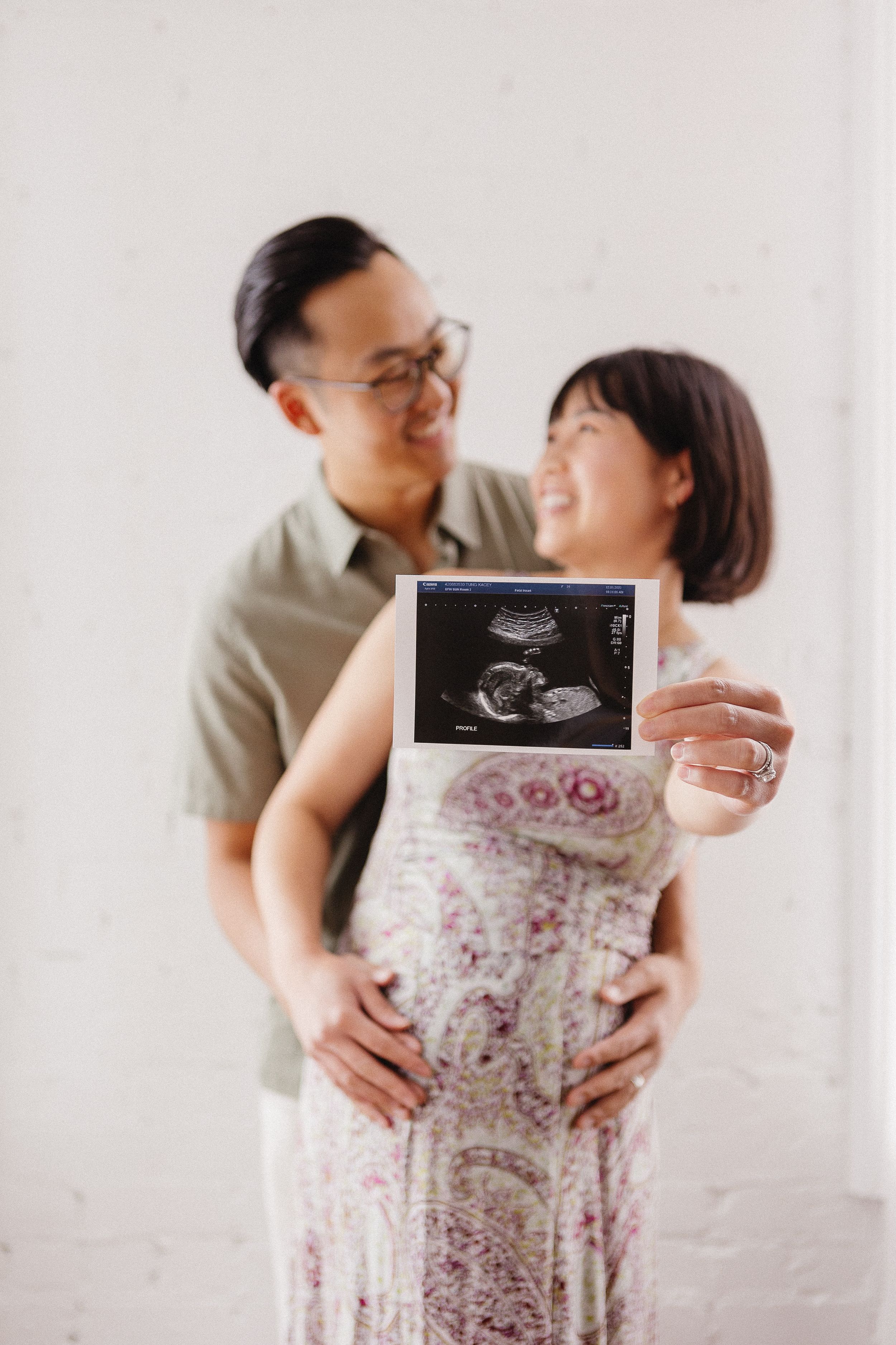 A couple shares intimate moments while holding ultrasound photos in a maternity photoshoot.