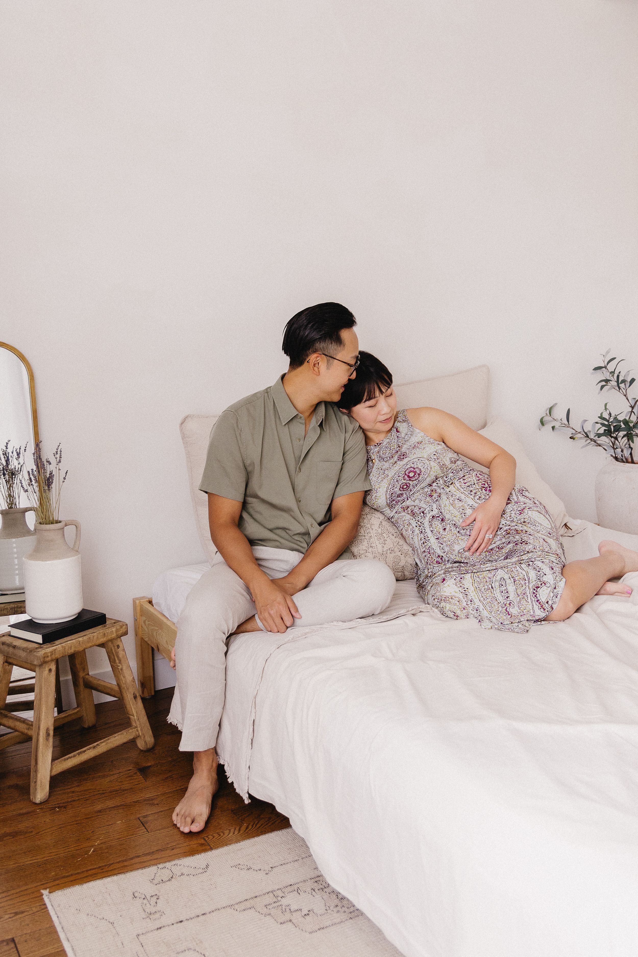 Couple lounging on white bed in minimalist bedroom with wooden accents.