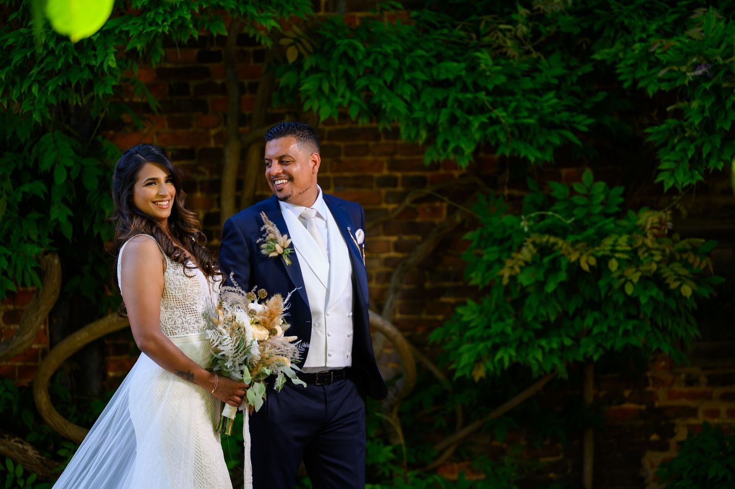 Wedding couple poses in a lush garden setting with dramatic lighting.
