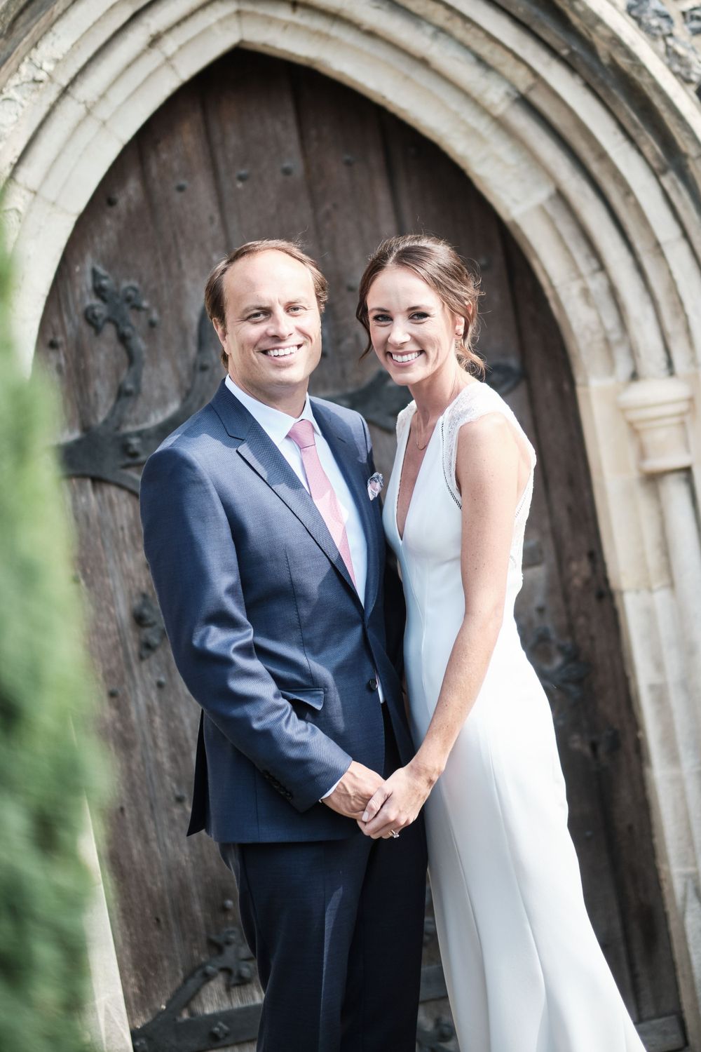 Wedding couple poses together in front of an ornate stone church archway.