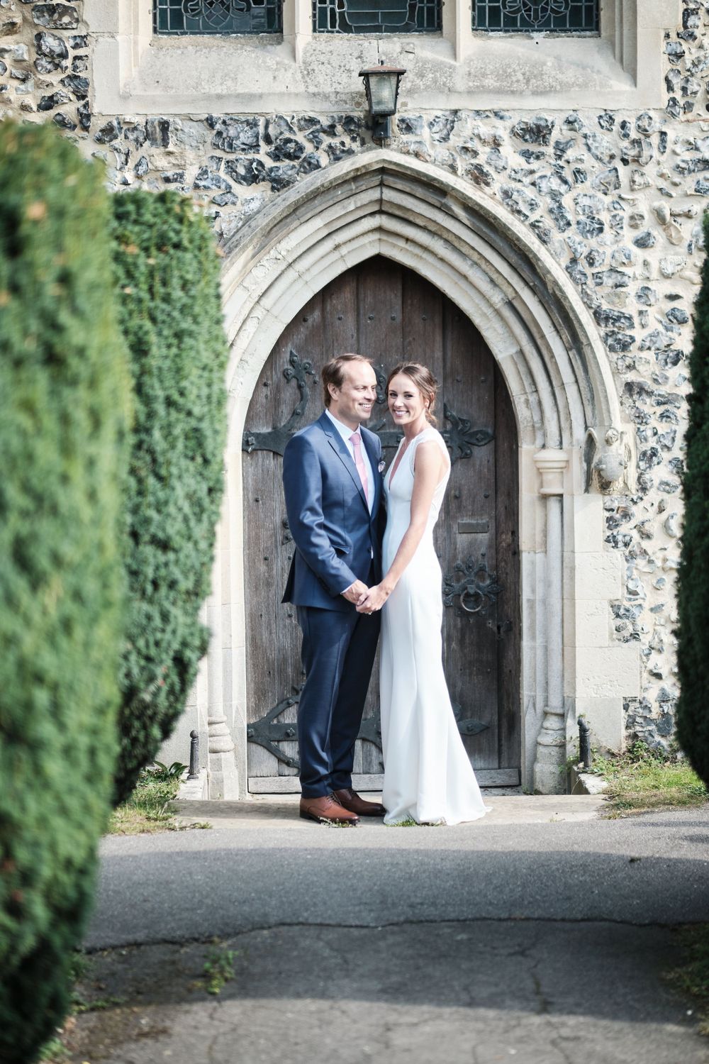 Elegant couple poses in front of gothic church doorway during wedding photoshoot.
