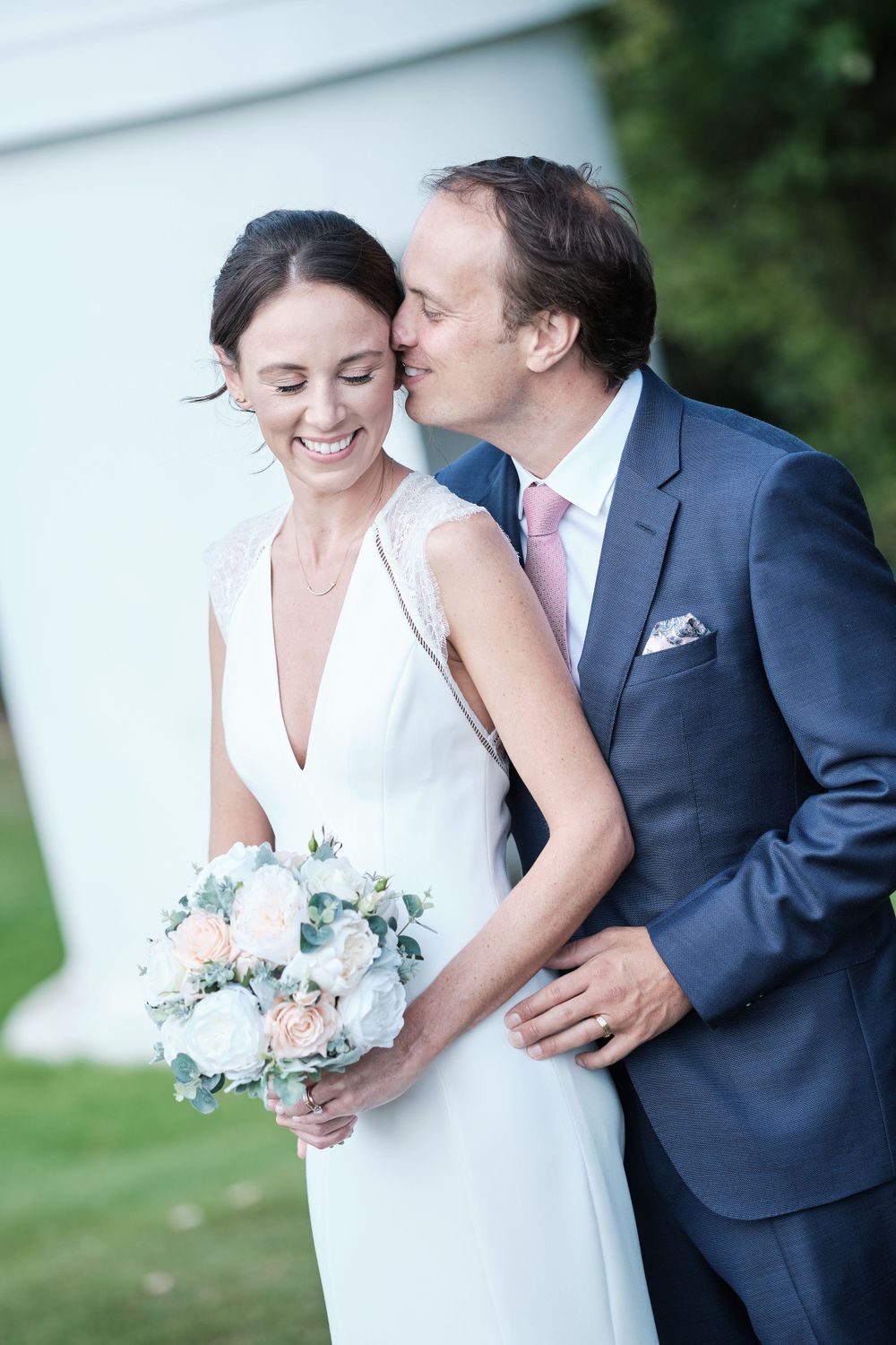 A tender wedding moment with the couple sharing laughter while holding a pastel bouquet.