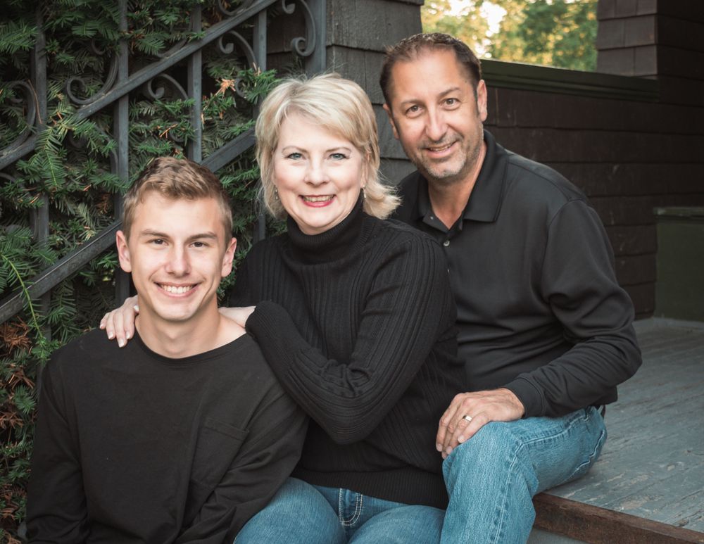 Family of three in black sweaters sitting on outdoor steps.