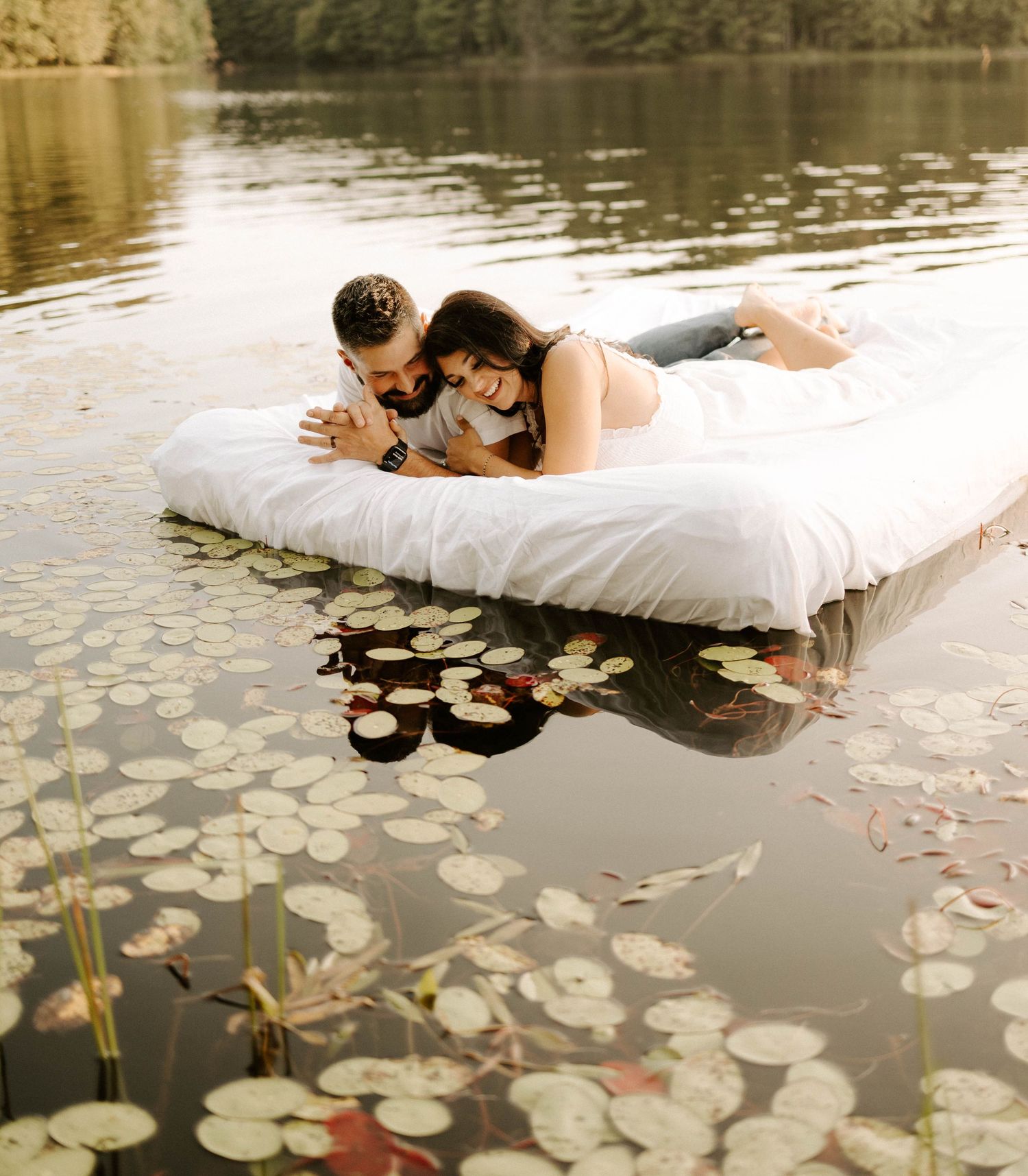 Couple laying on floating mattress in lily pad covered pond.