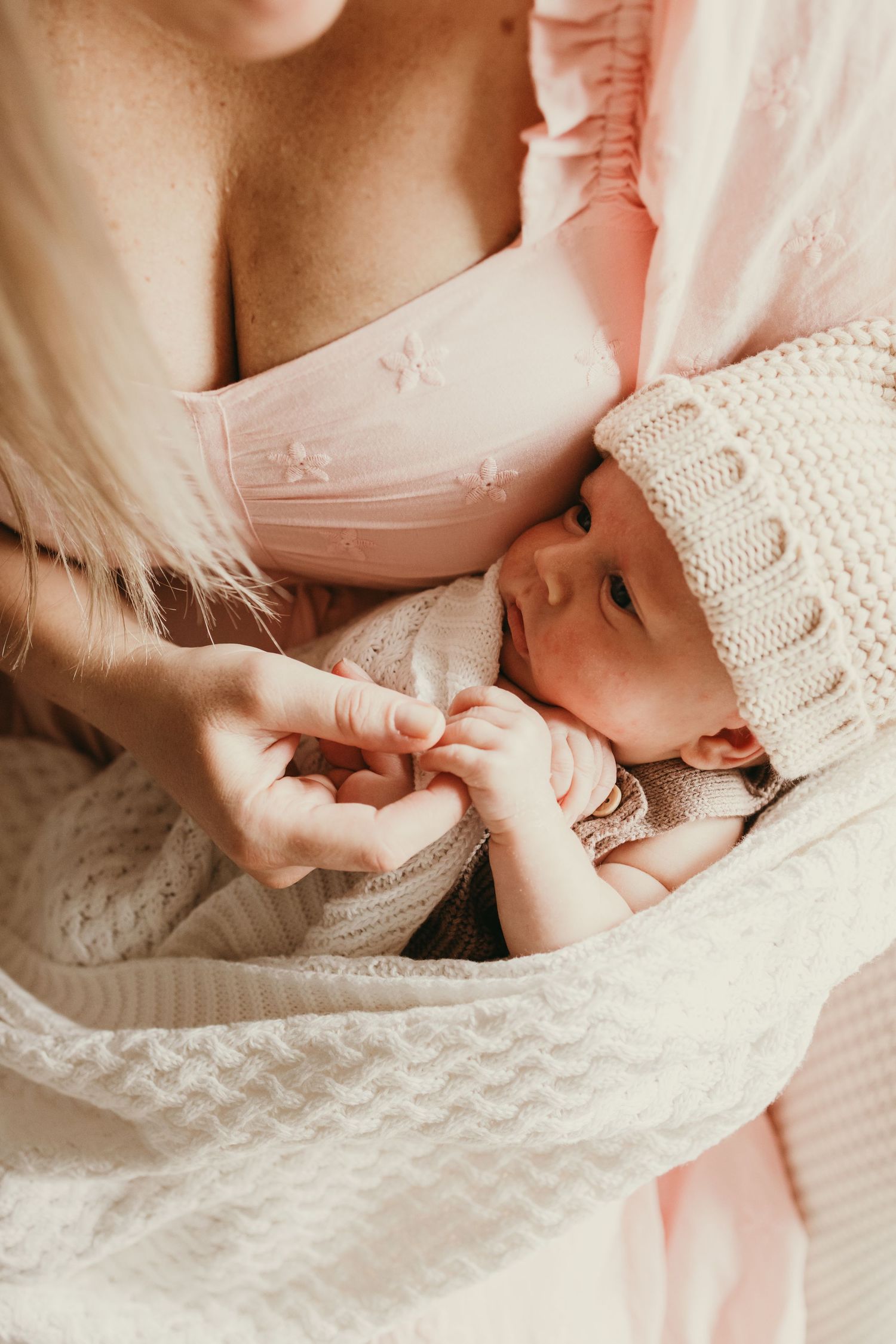 A newborn baby wearing a knitted white hat swaddled in soft textiles.