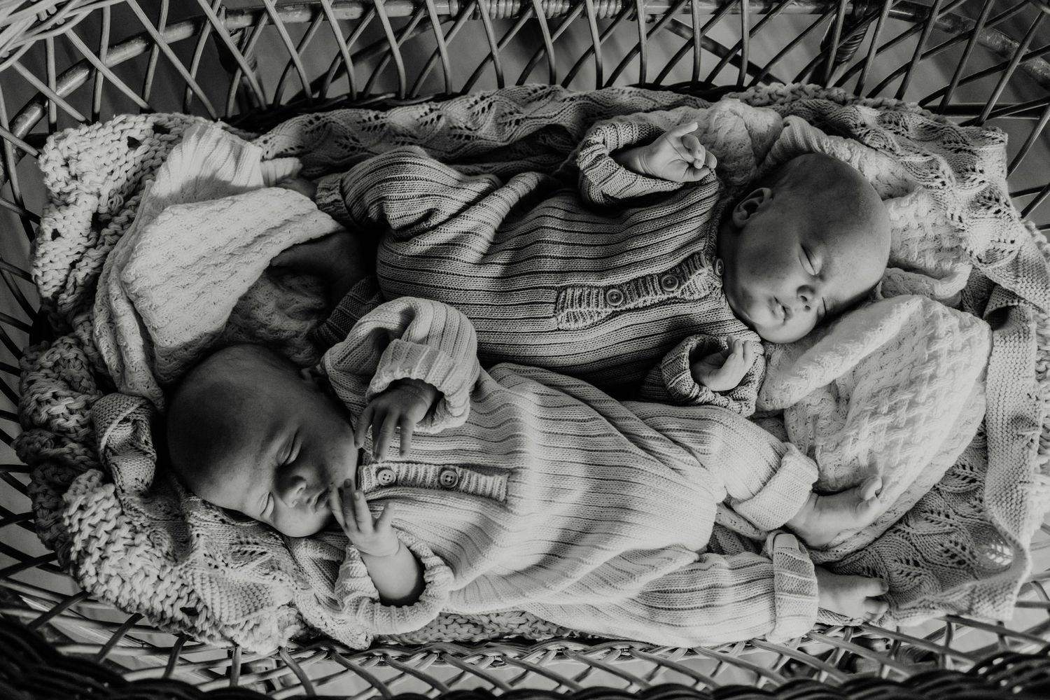 Two sleeping infants lying together in a bassinet wearing matching striped outfits.