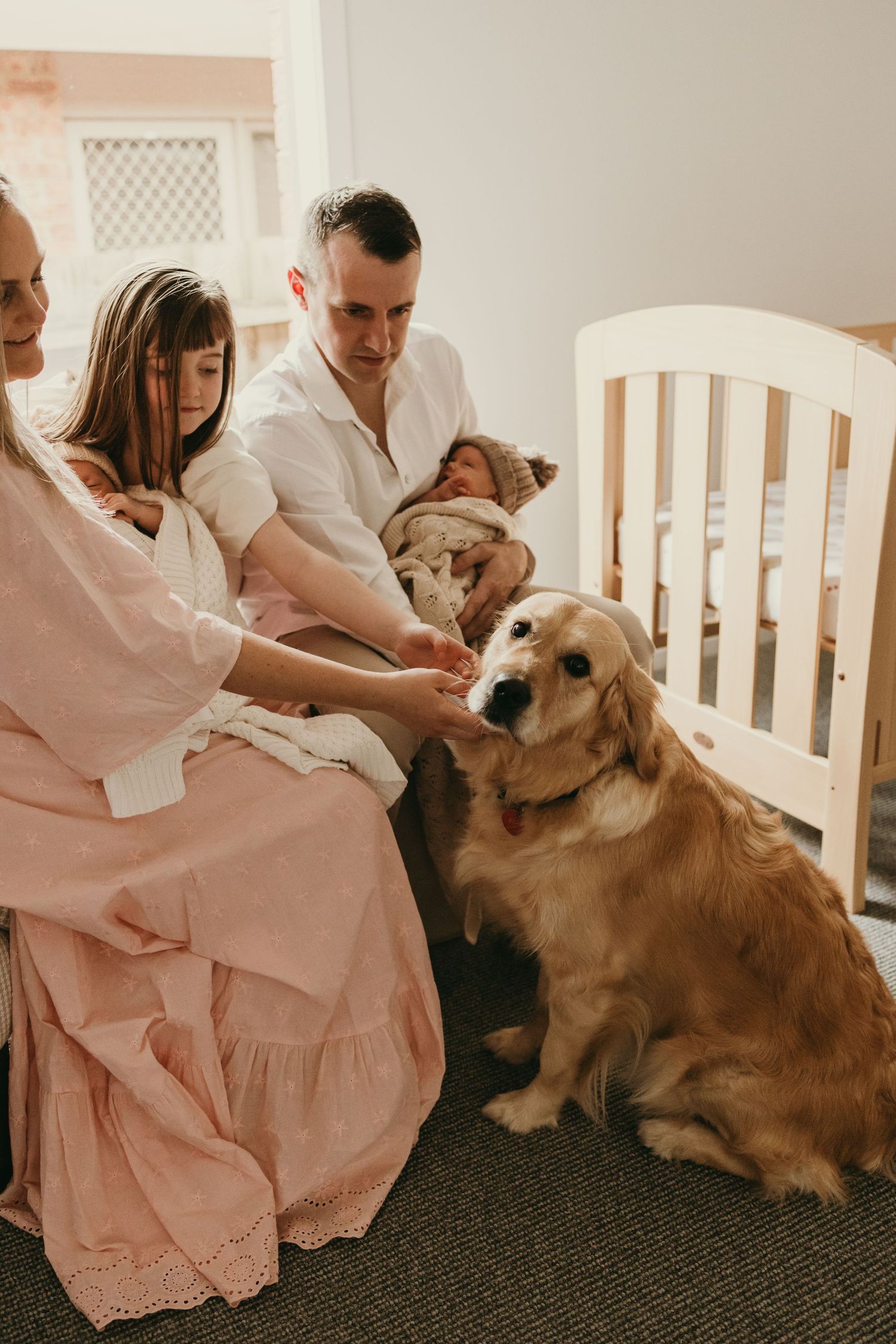 A cozy family scene in a nursery with a golden retriever beside a white crib.