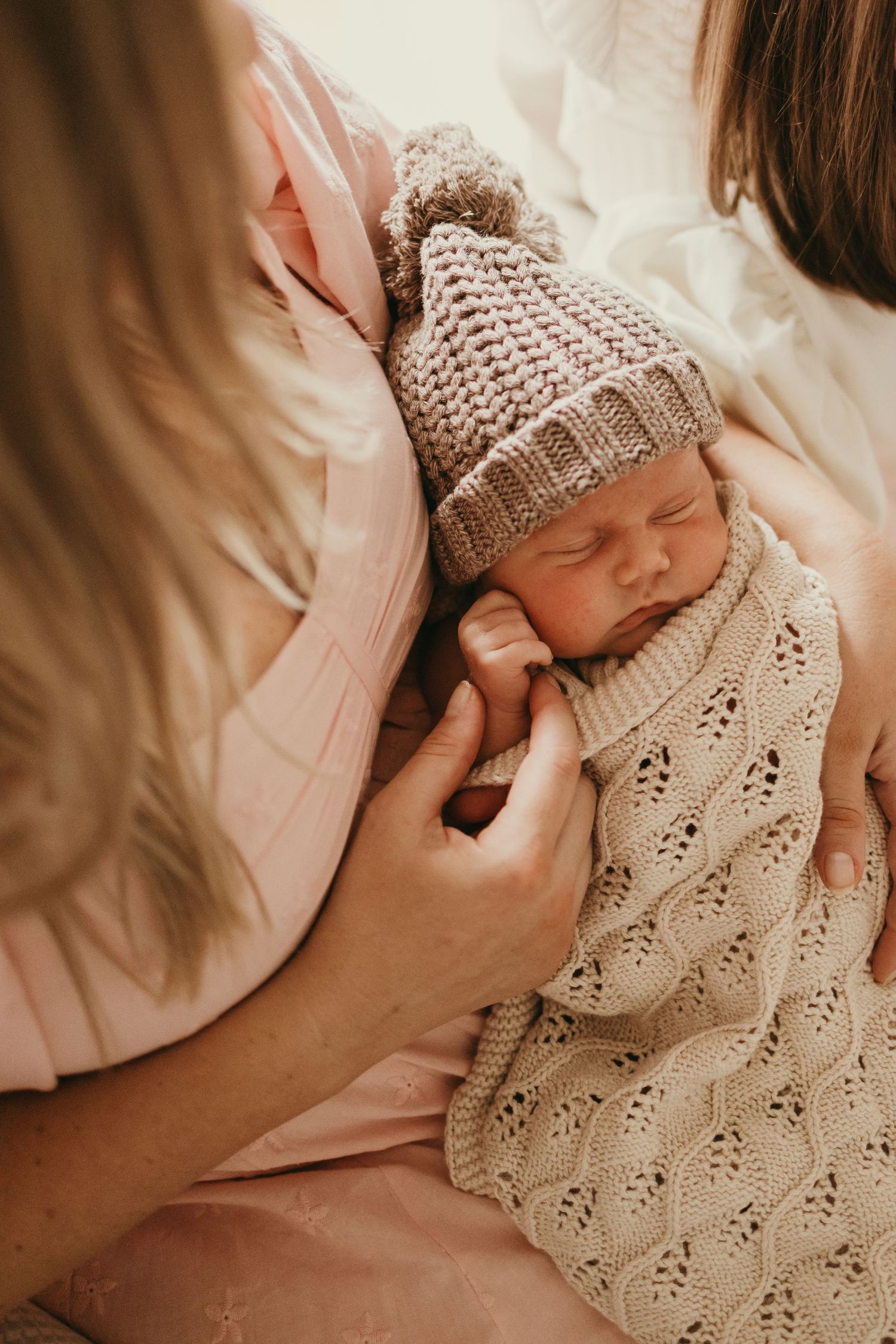 Close-up of sleeping newborn wearing knitted beige hat and blanket.