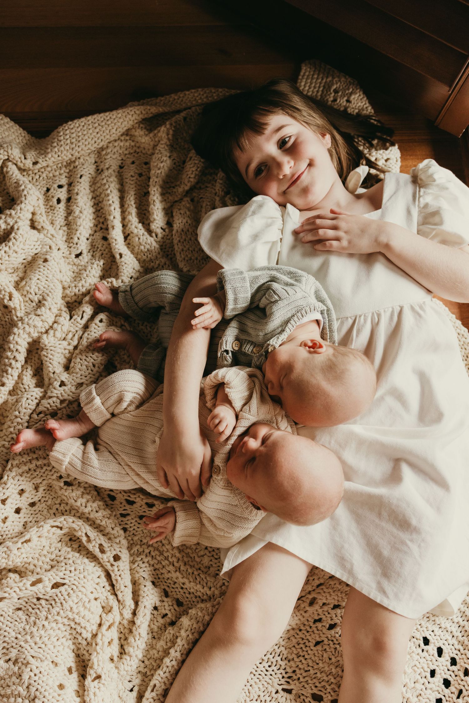 Siblings sharing a peaceful moment on a crocheted blanket in warm natural lighting.