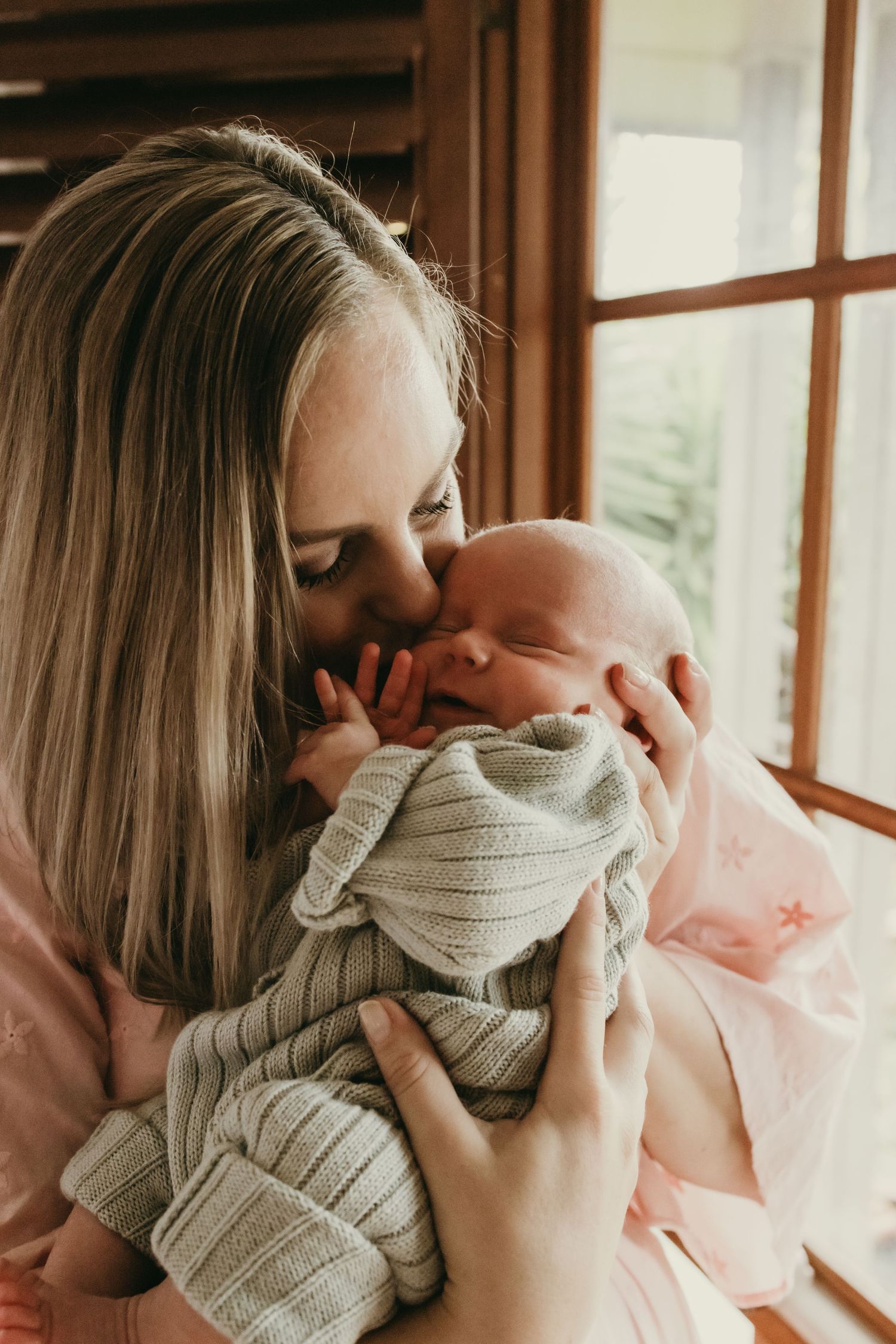 Intimate portrait showing gentle embrace of a sleeping newborn wrapped in soft gray knit fabric.