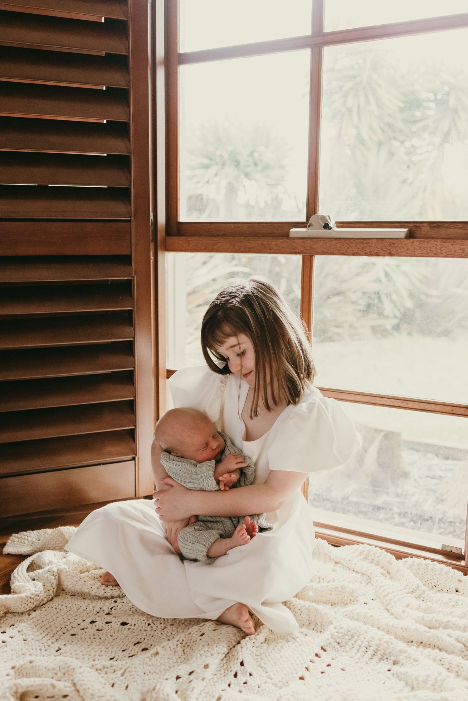 Serene scene by a window showing a tender moment with a newborn on a textured blanket.