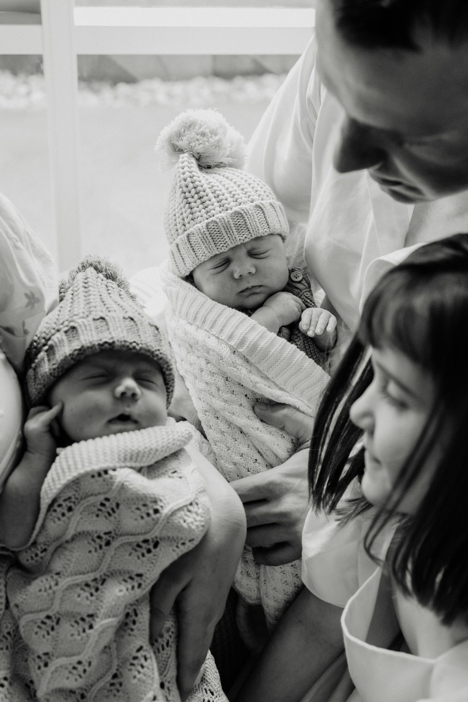 Black and white portrait of sleeping twins in matching knit hats with family.