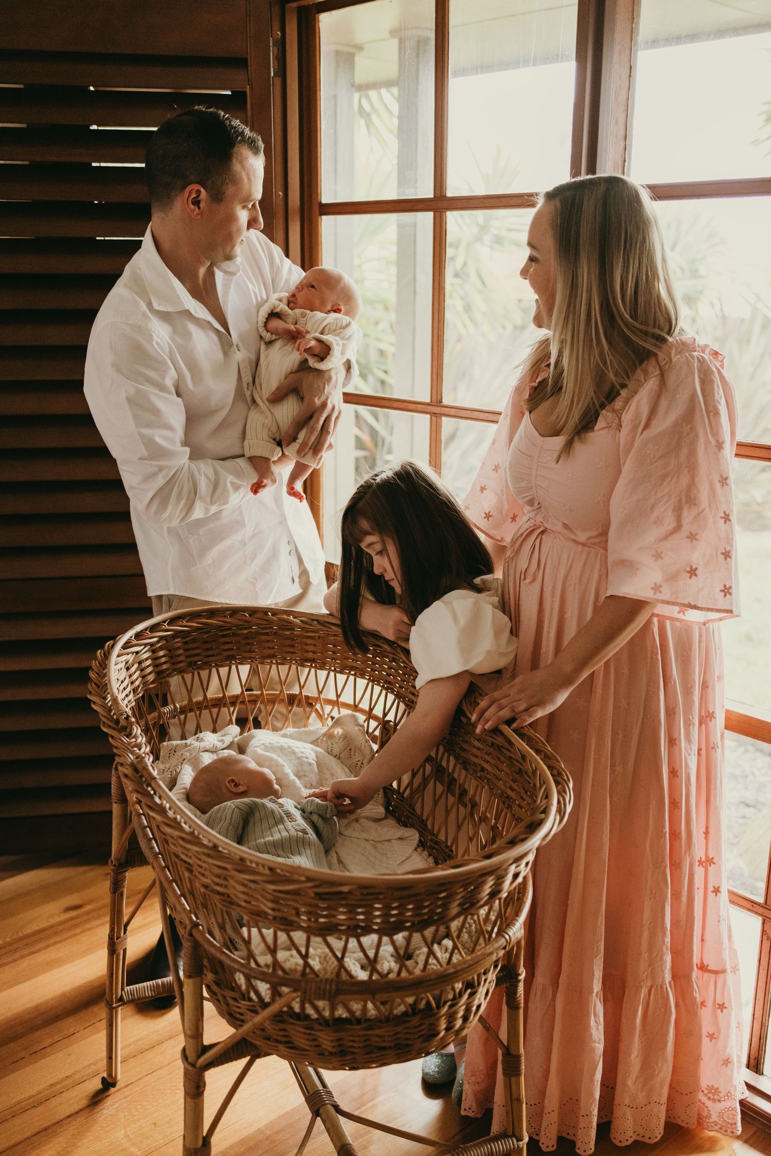 A family gathered around a wicker bassinet near a window in warm natural light.