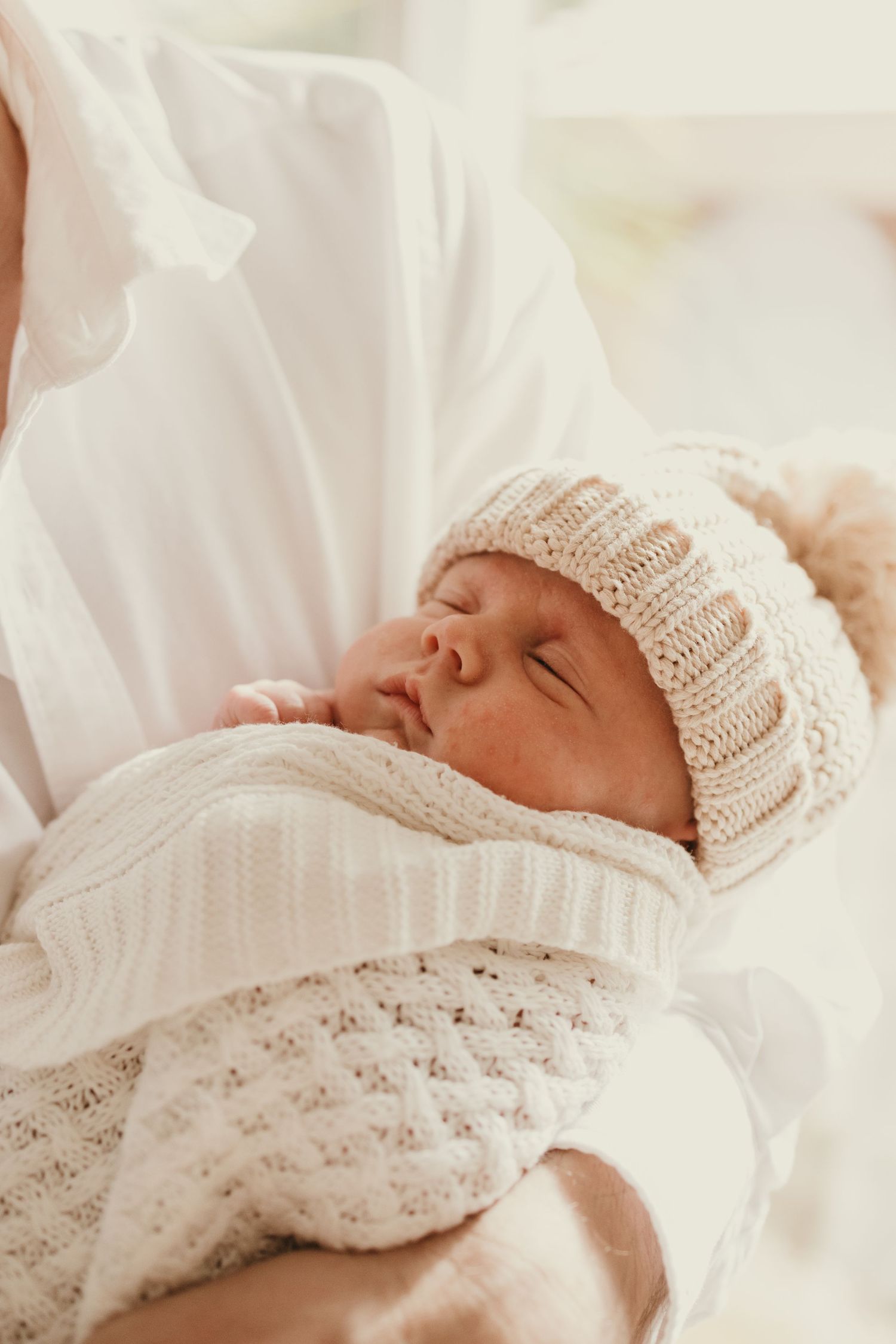 Peaceful newborn baby sleeping in cream knitted hat and wrap against soft white background.
