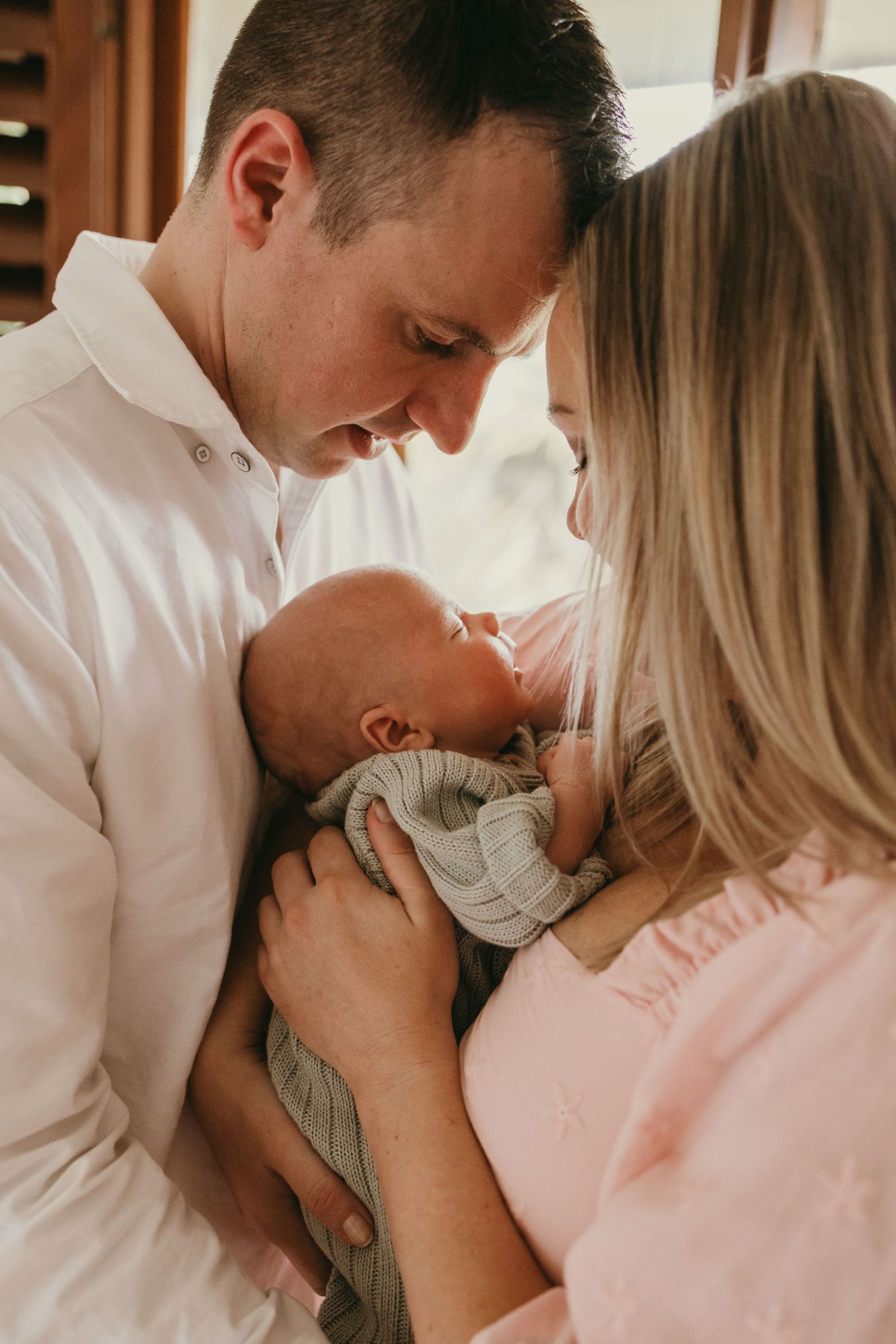 Parents sharing an intimate moment with their newborn baby in soft natural lighting.