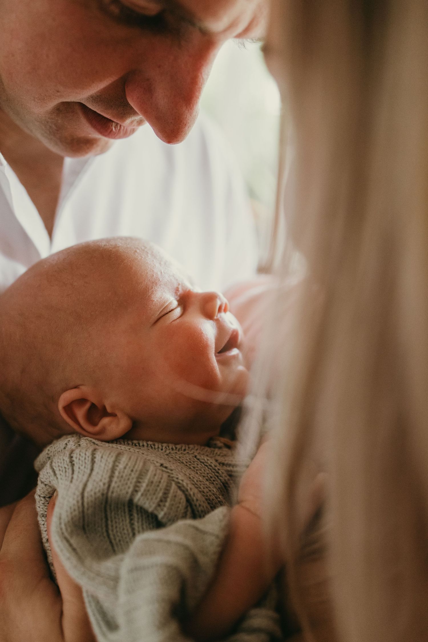 Close up side profile of tender moment between parent and sleeping newborn in soft light.