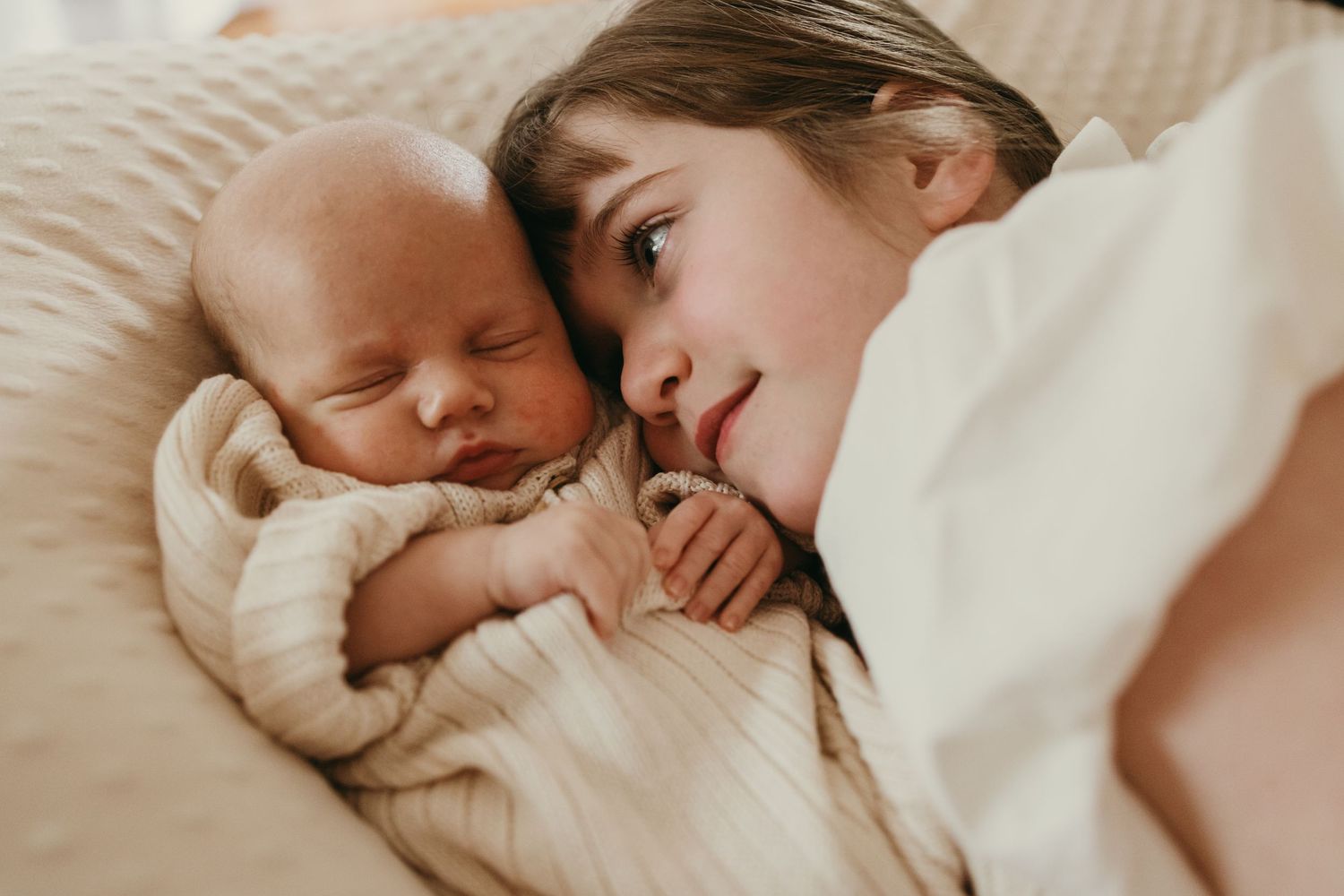 Mother and baby sharing a tender moment while resting together on white bedding.