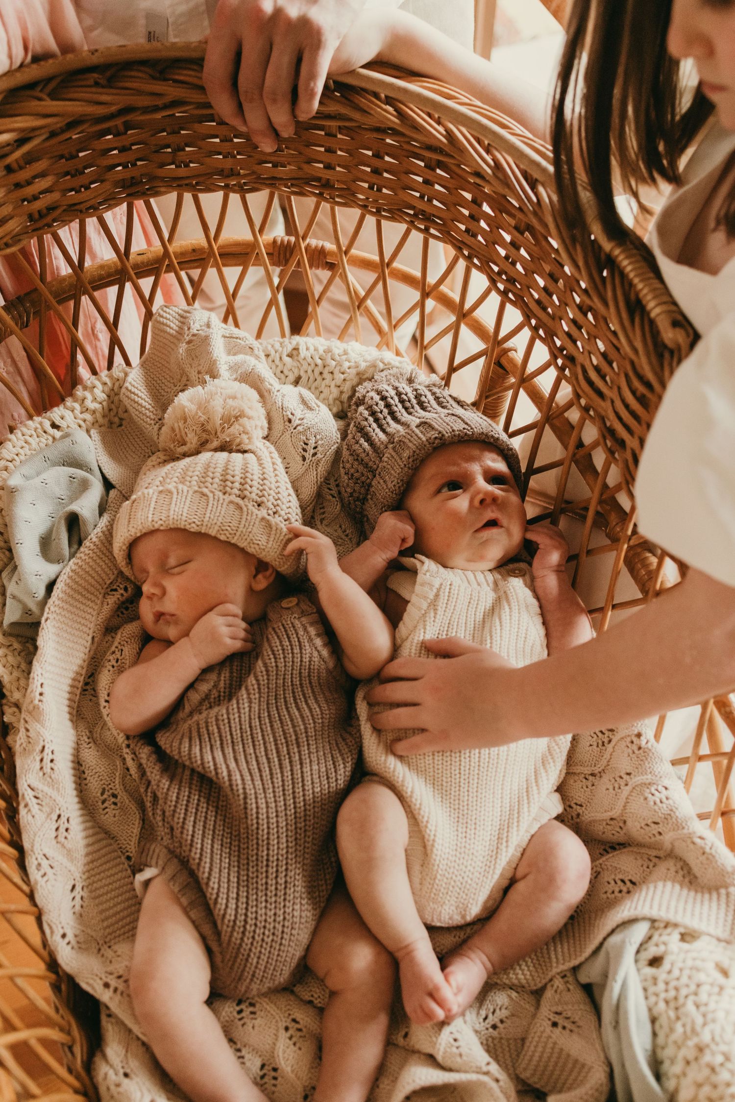 Twins in matching knit outfits lying in handwoven wicker bassinet.
