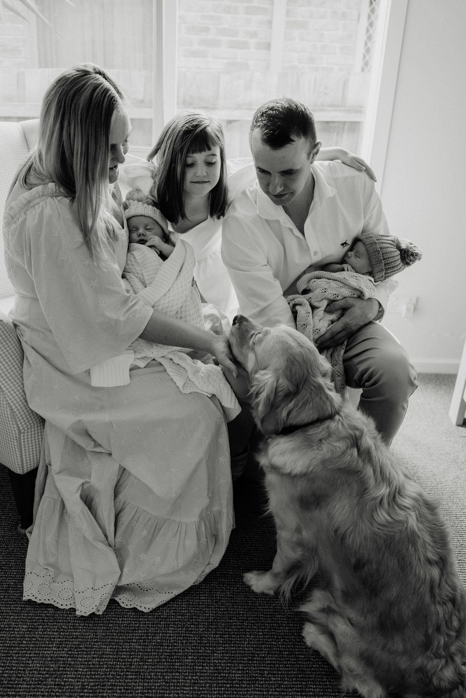 A black and white family portrait with a golden retriever in a bright nursery setting.