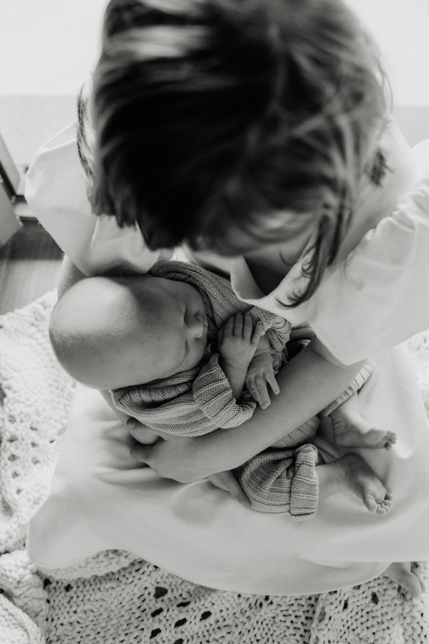 Black and white overhead shot of tender moment with sleeping infant on lace blanket.