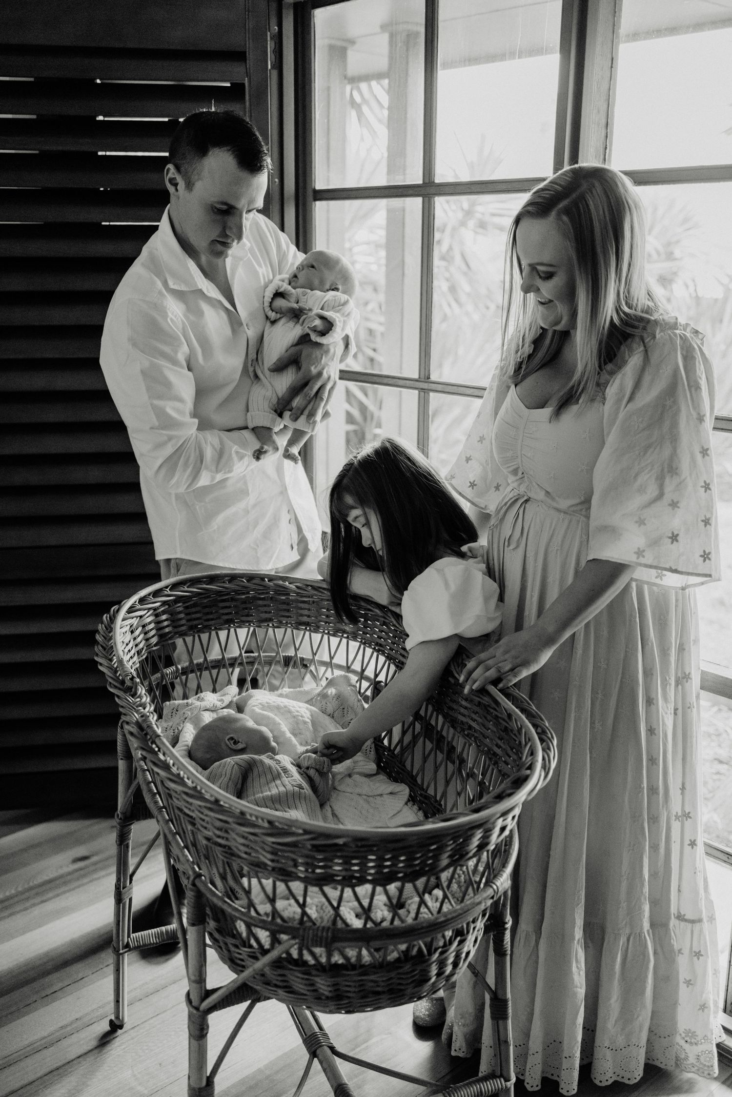 Black and white photo of parents looking at their newborn in a vintage wicker bassinet.