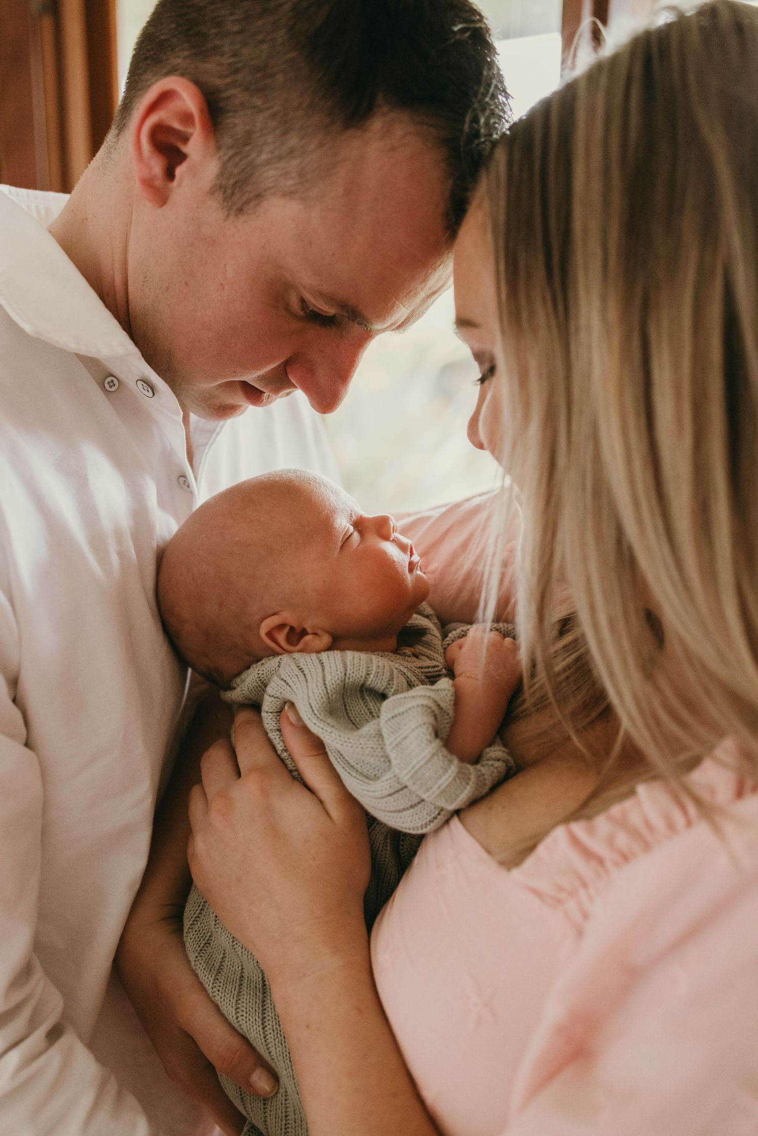 Close up of parents gazing lovingly at their newborn baby dressed in gray.