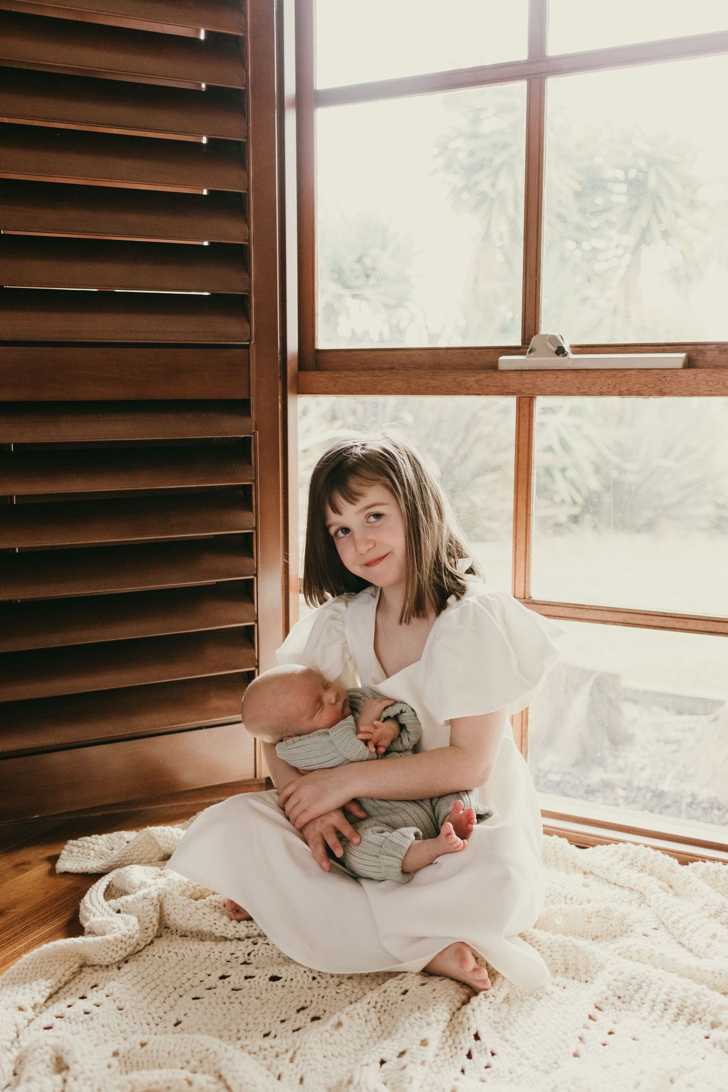 Peaceful moment captured by window light as caregiver sits with infant on crocheted blanket.