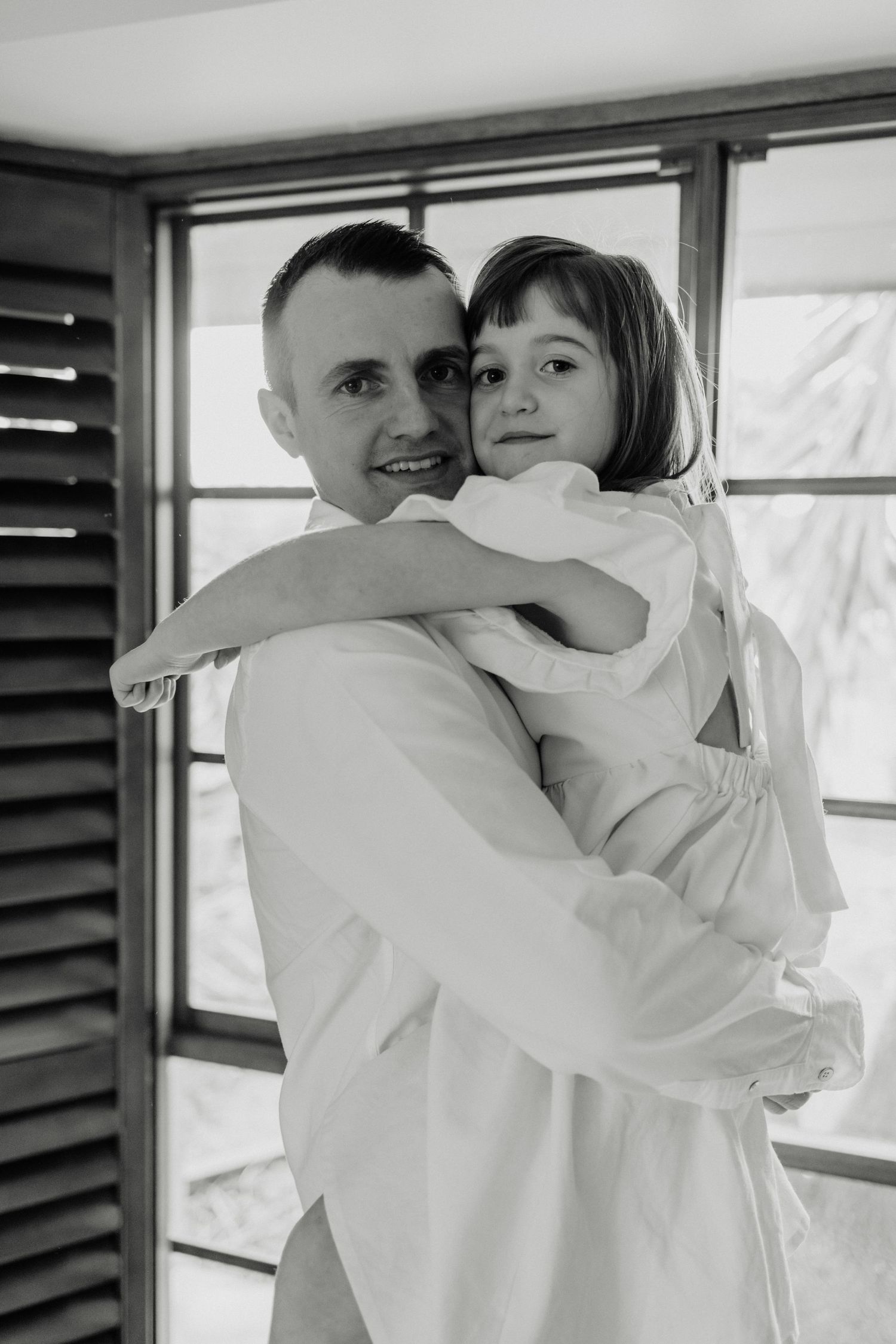 Black and white portrait by window with wooden shutters.