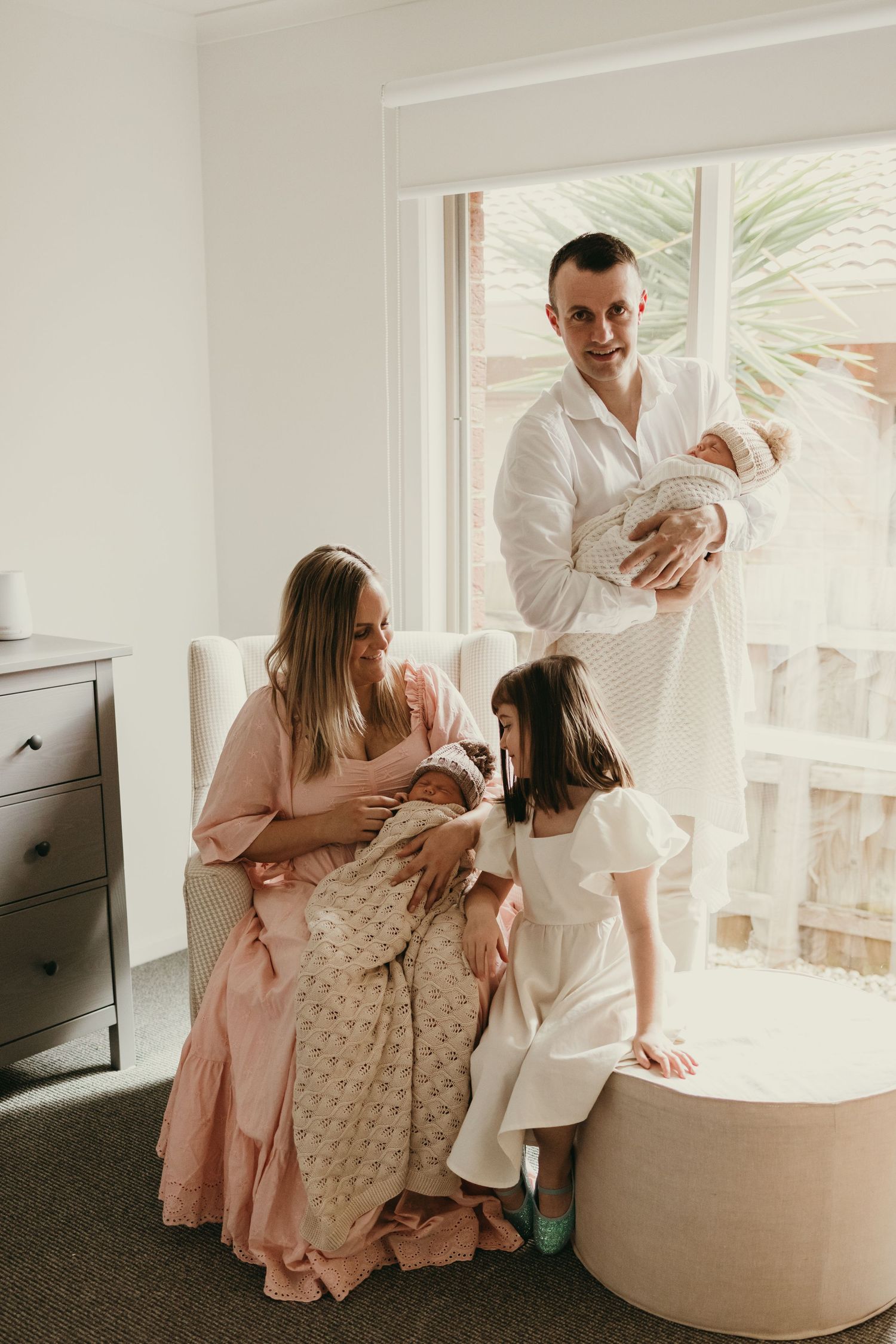Bright modern nursery scene with family gathering around newborn babies.
