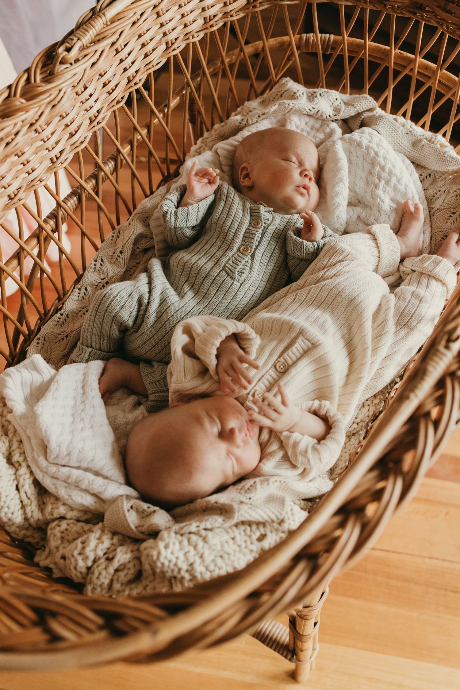 Two sleeping infants in matching sweaters nestled in a woven rattan basket.