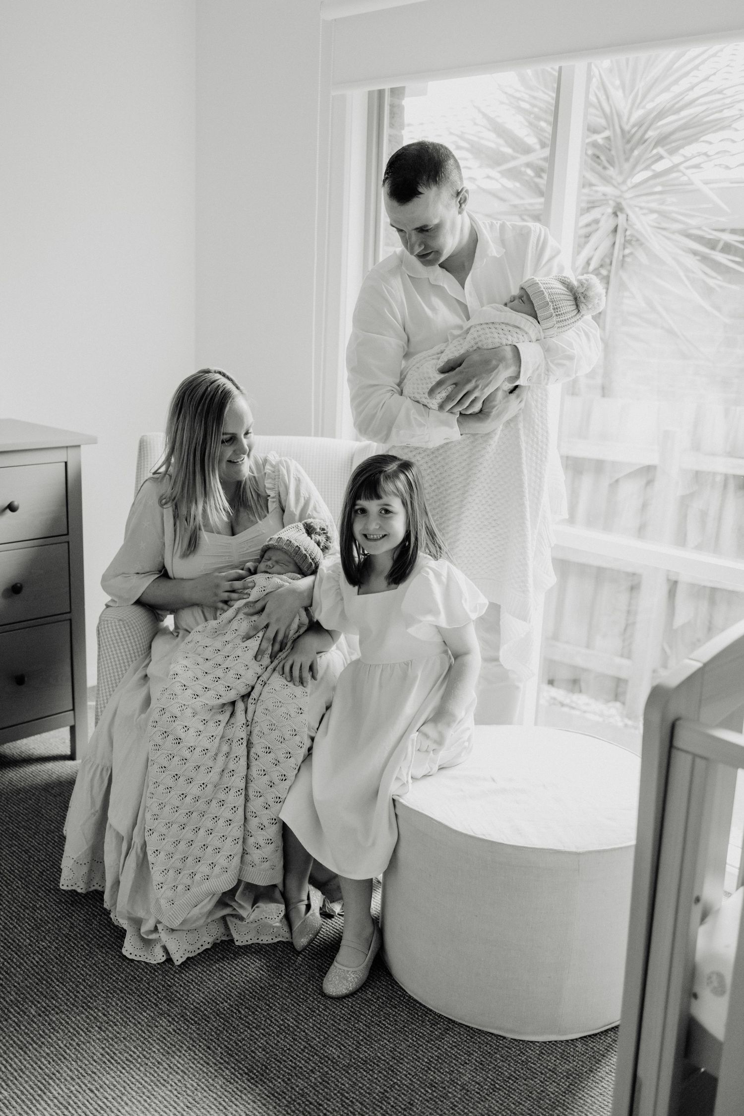 Black and white capture of tender family moment in minimalist nursery setting.