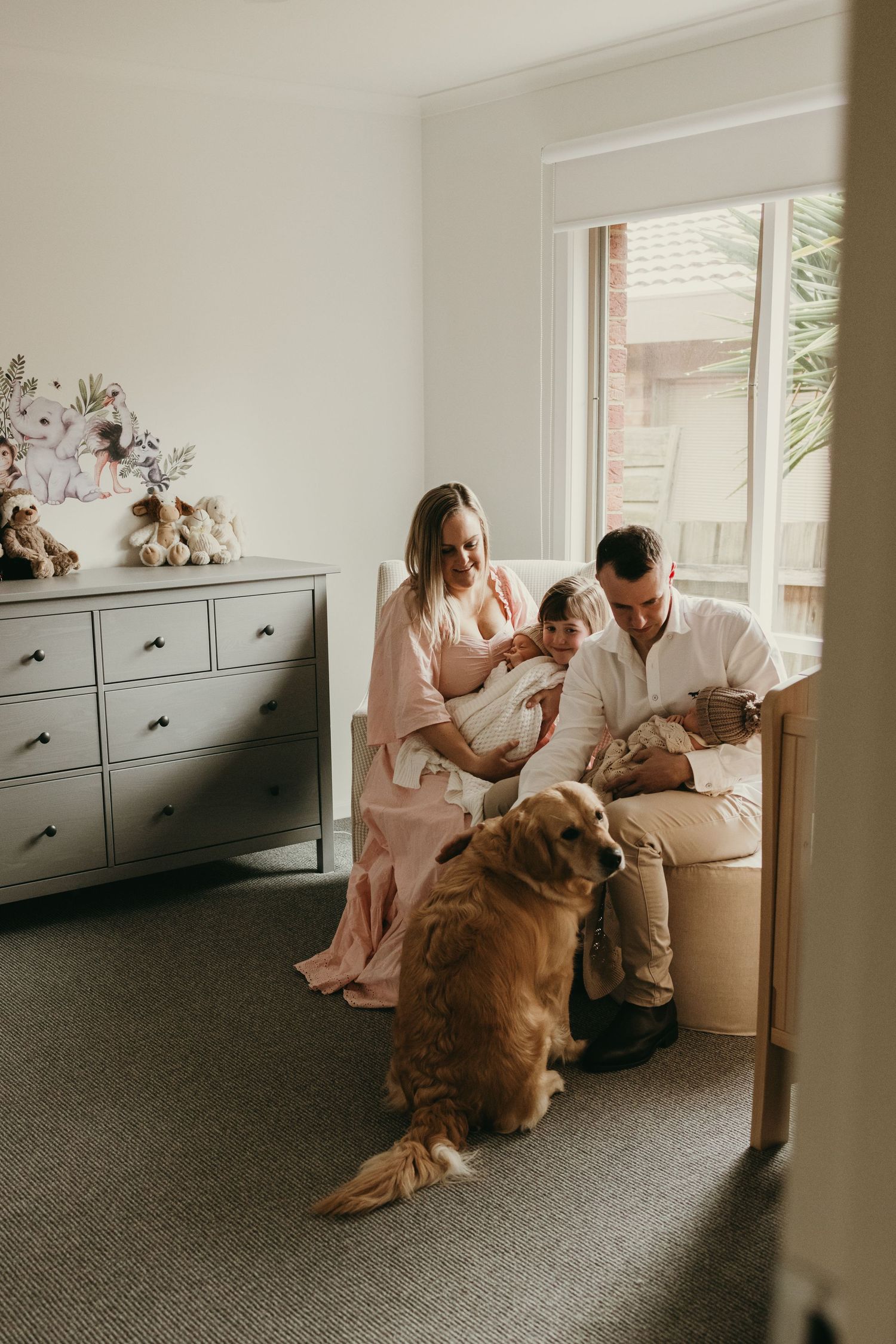 A family sits together in a nursery with their golden retriever by a window.