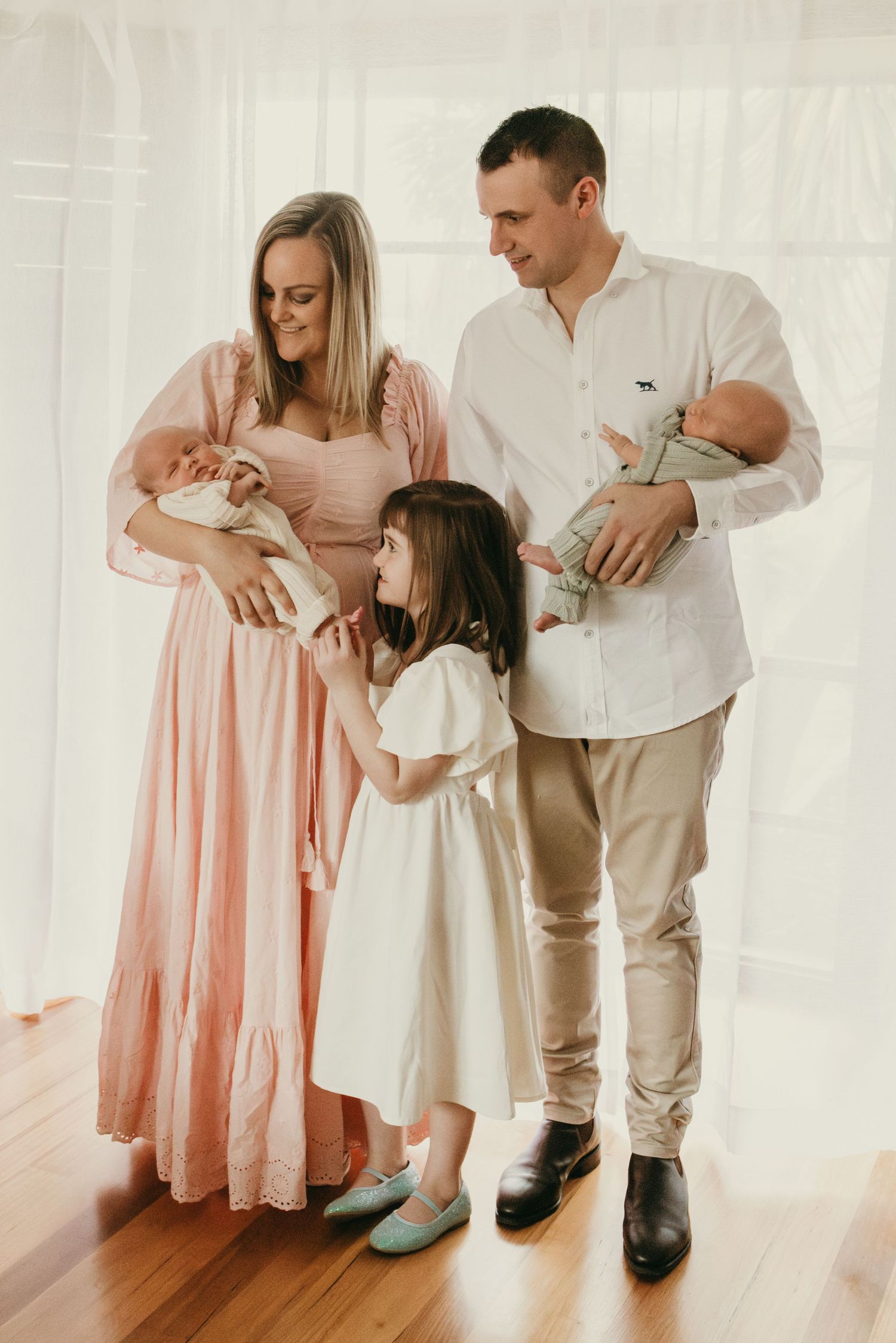 Family portrait in white room with hardwood floors.