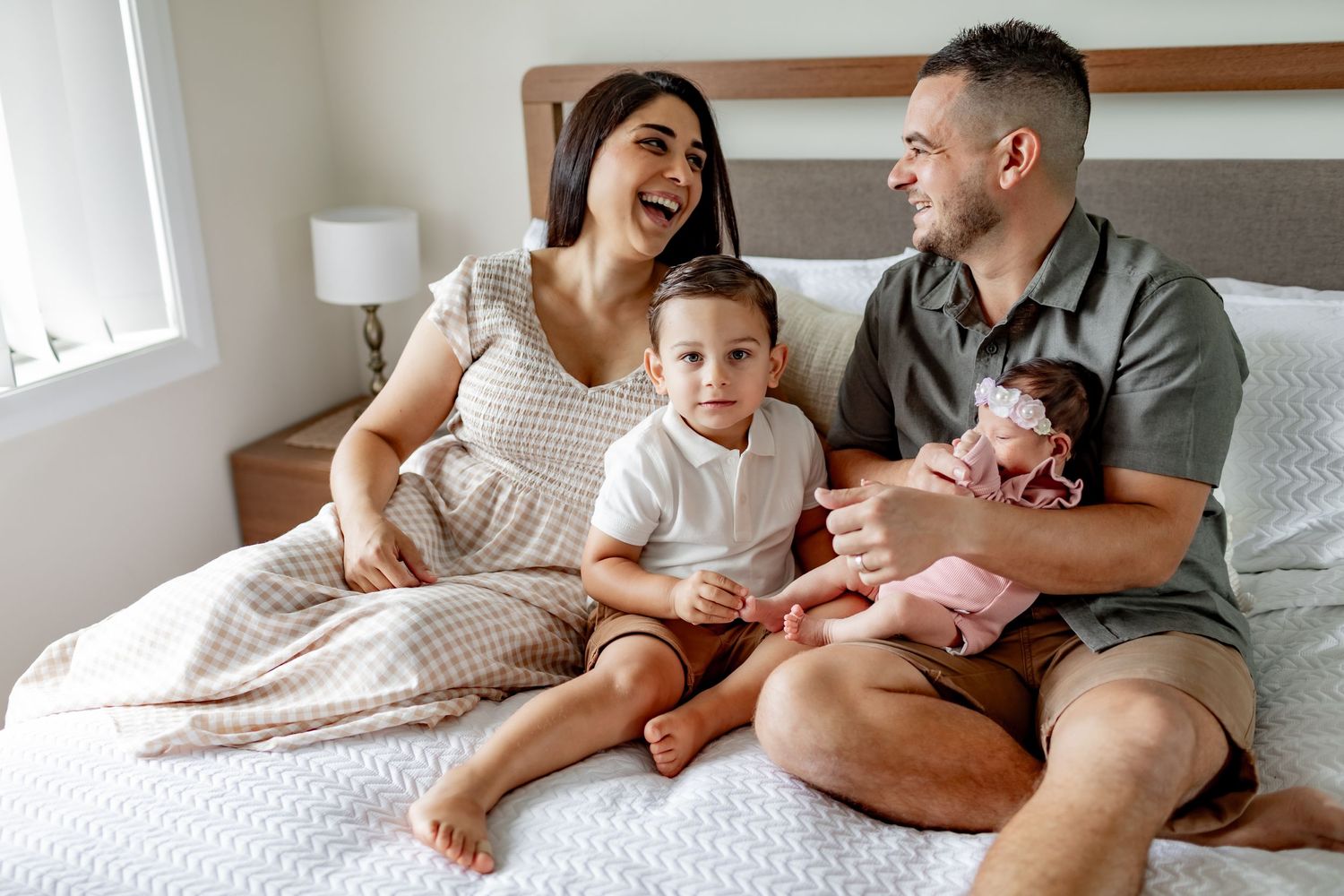 Family sharing joyful moments together while sitting on bed in matching white outfits.