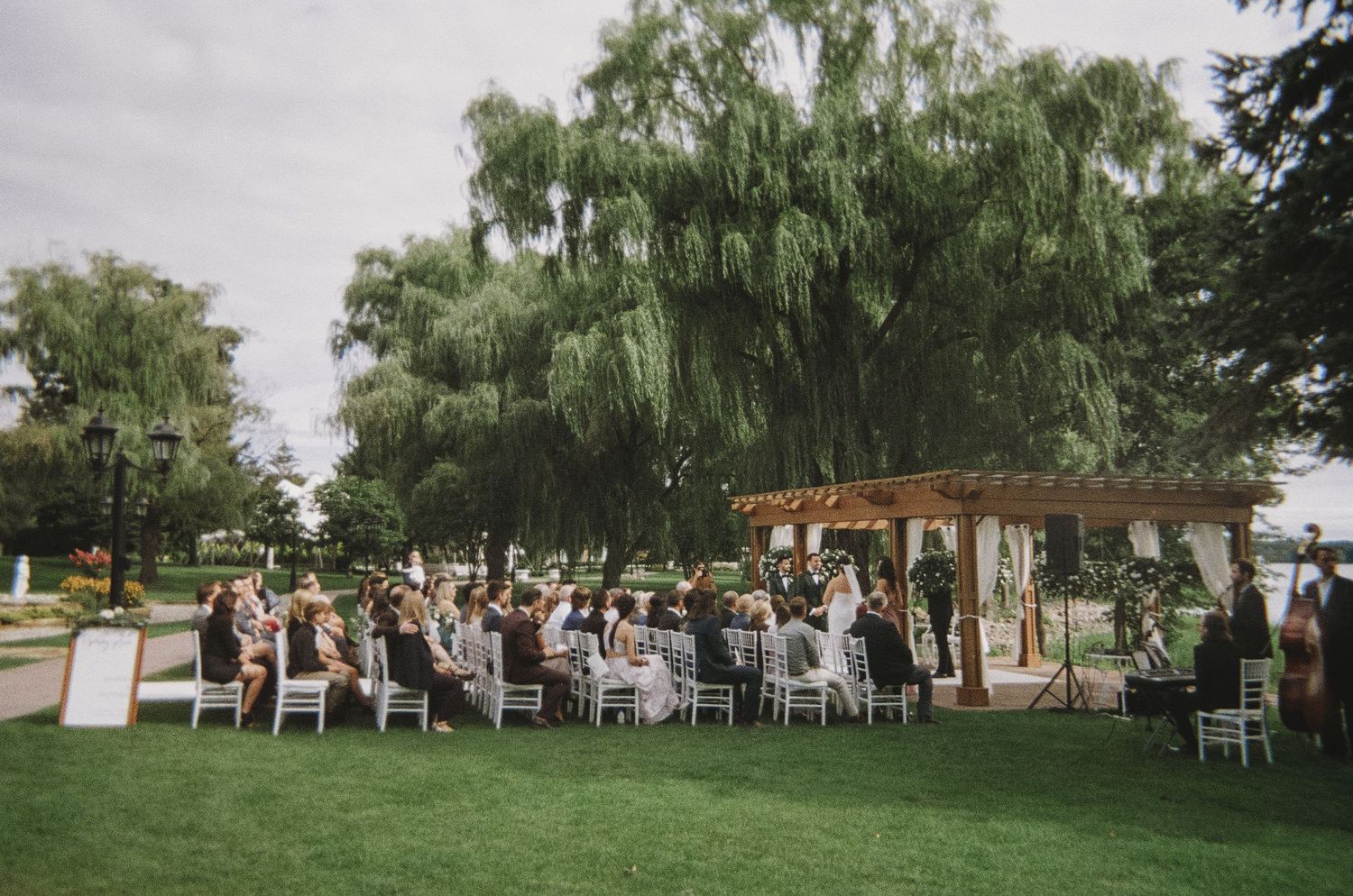 An outdoor wedding ceremony setup with white chairs under willow trees.